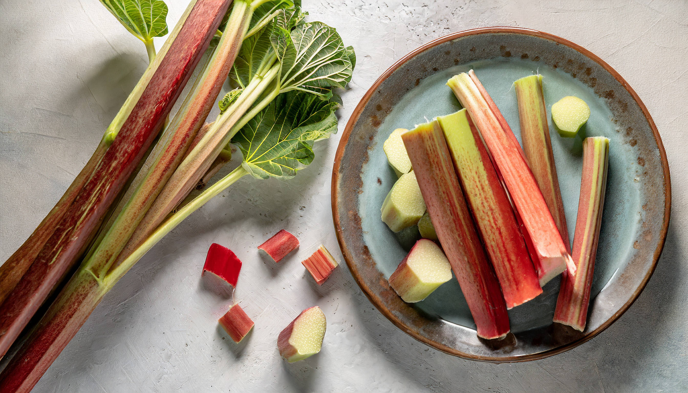 Frischer Rhabarber, ganz und geschnitten, auf Teller und Arbeitsfläche.