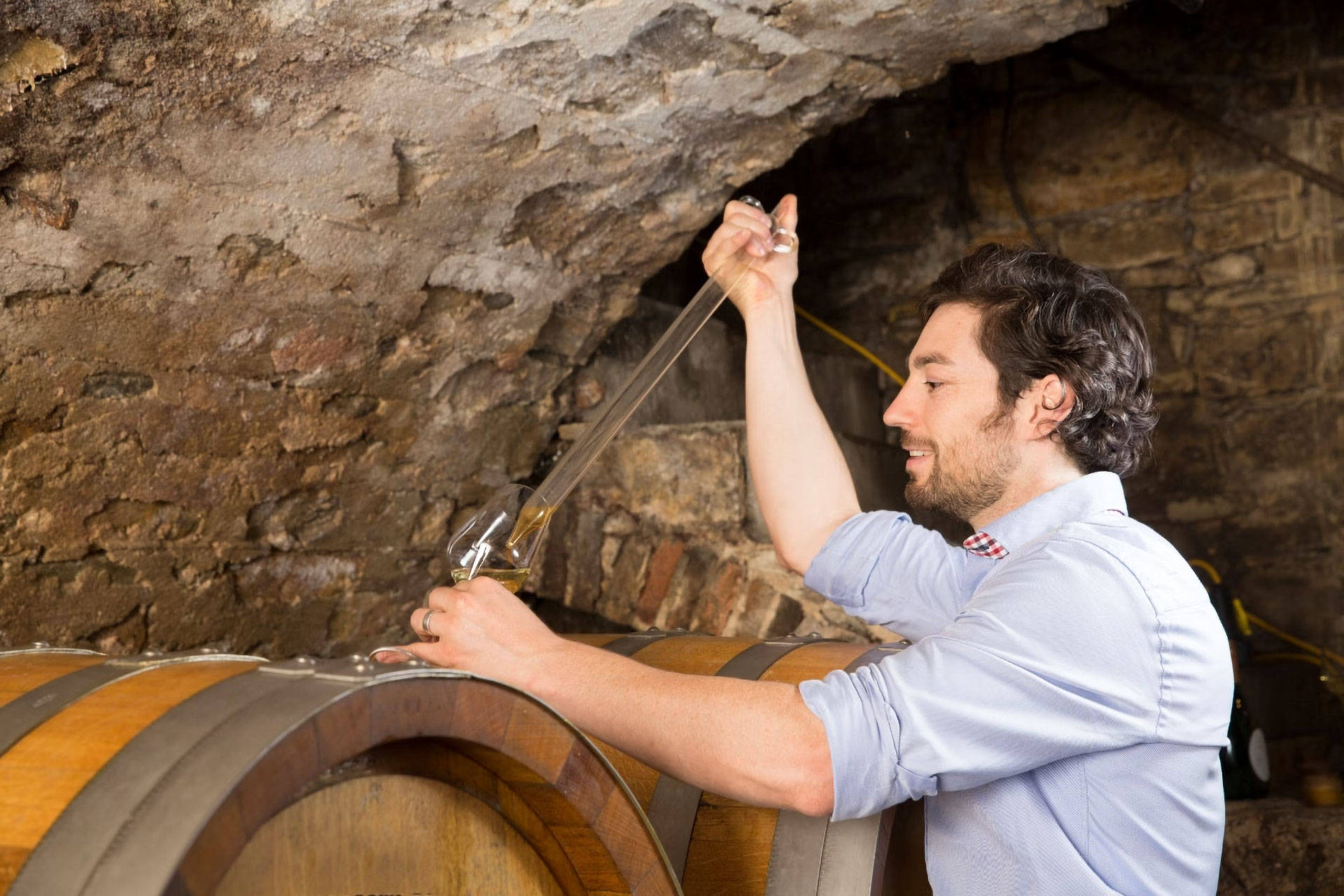 Winzer nimmt eine Probe Wein aus einem großen Holzfass im Keller.