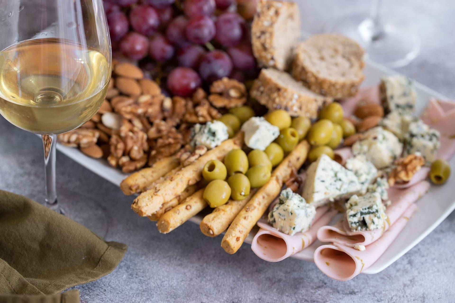 Gemischte Vorspeisenplatte mit Oliven, Käse und Wurst. Daneben ein Glas Riesling.