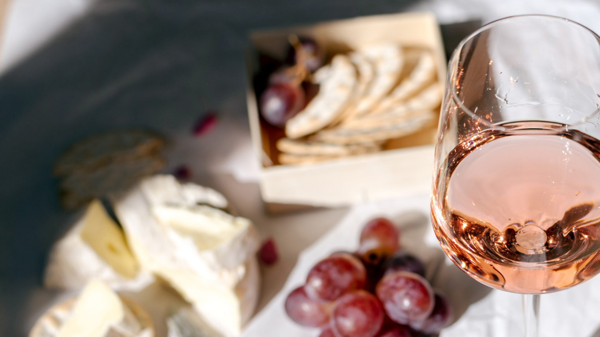 Roséwein, Käse, Trauben und Cracker auf weißem Tuch.