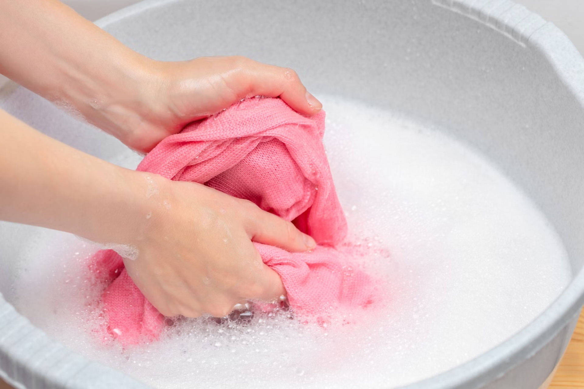 Eine Person wäscht ein rosa farbenes Kleidungsstück in einer Schüssel mit Gallseife.