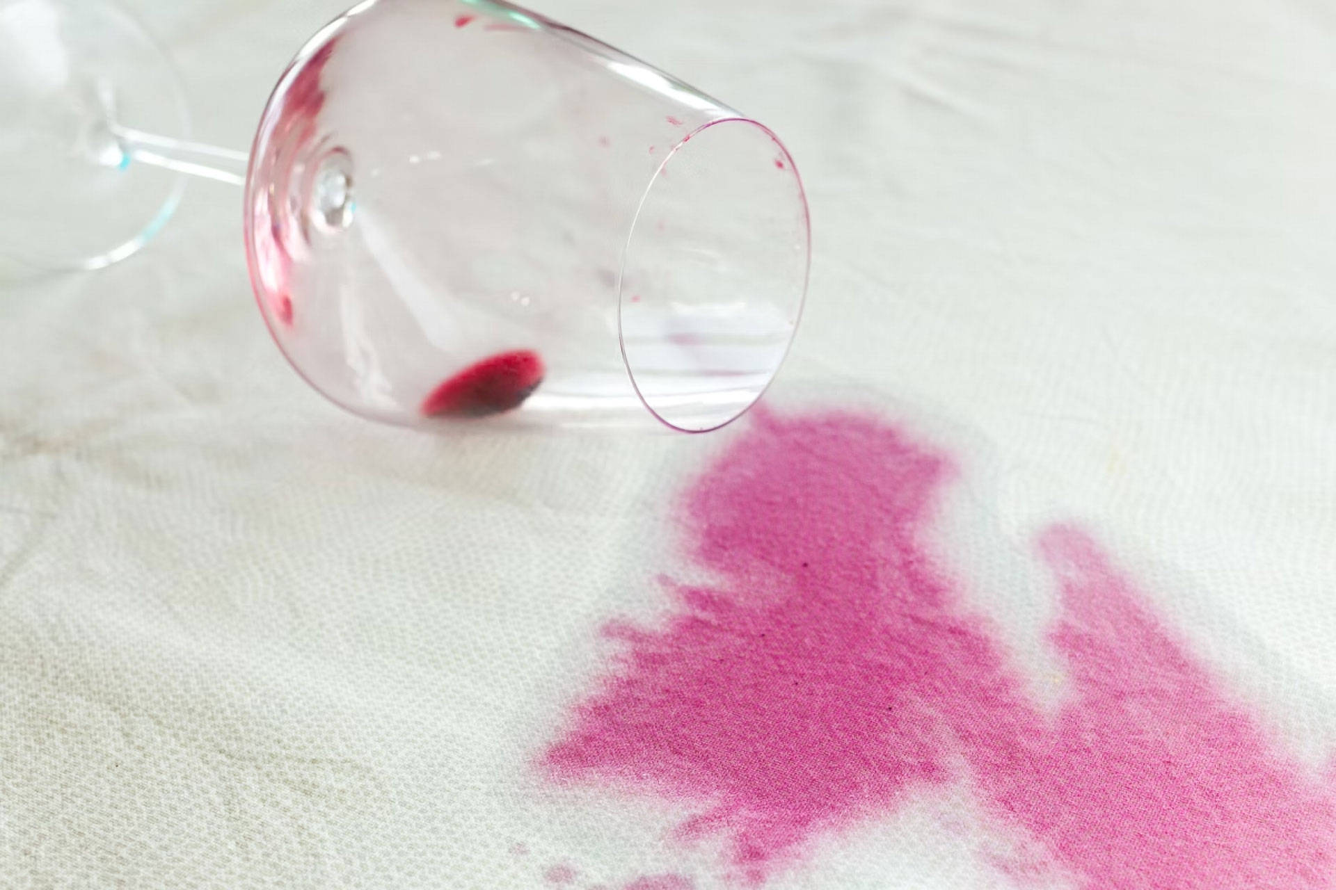 Ein umgefallenes Glas Rotwein hinterlässt einen Fleck auf einem weißen Stoff.