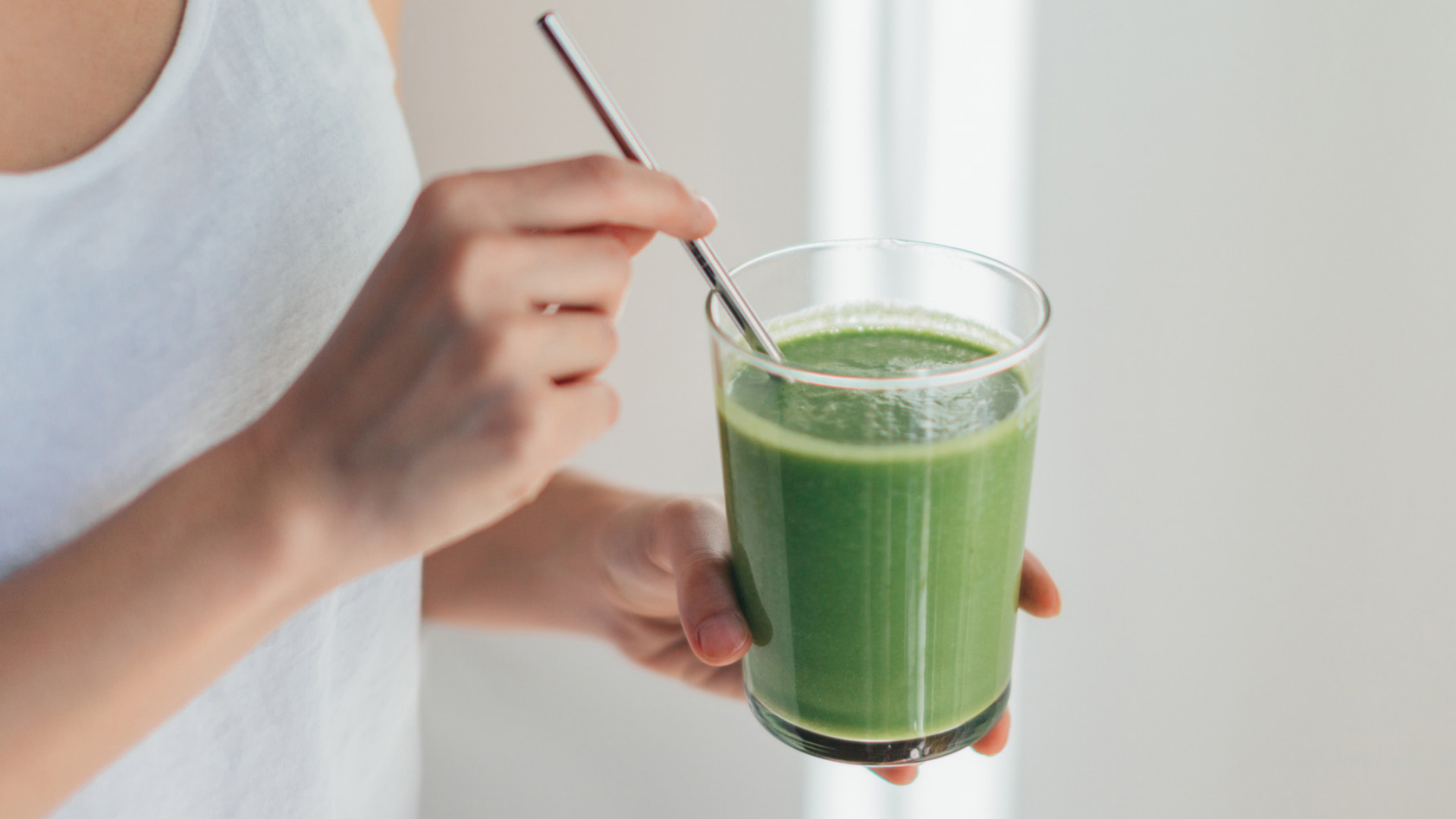 Frau hält grünen Smoothie mit Metallstrohhalm.