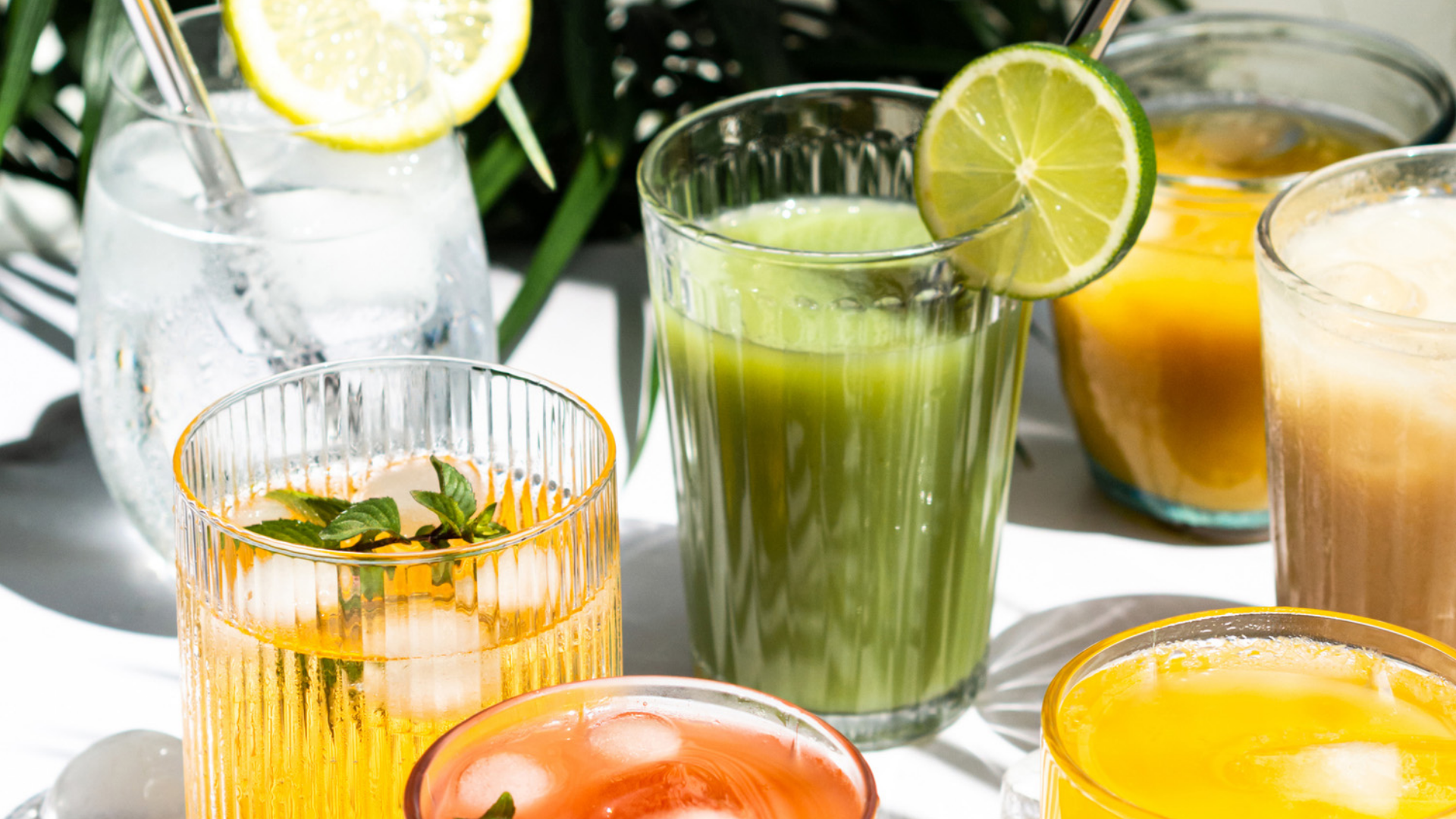 Mehrere Gläser mit farbigen Säften und Eiswürfeln.