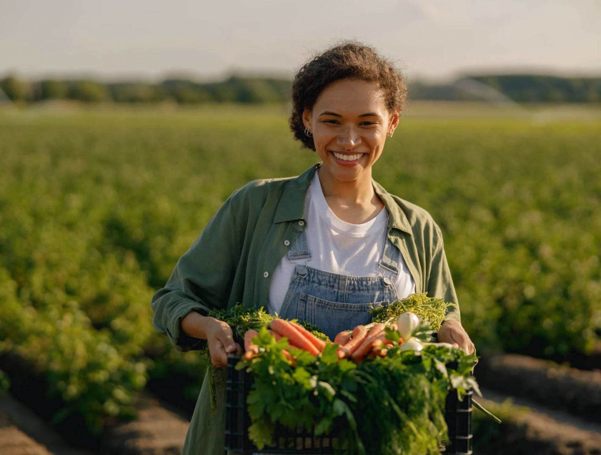 Ein Frau trägt ein Kiste mit frisch geernteten Möhren vom Feld.