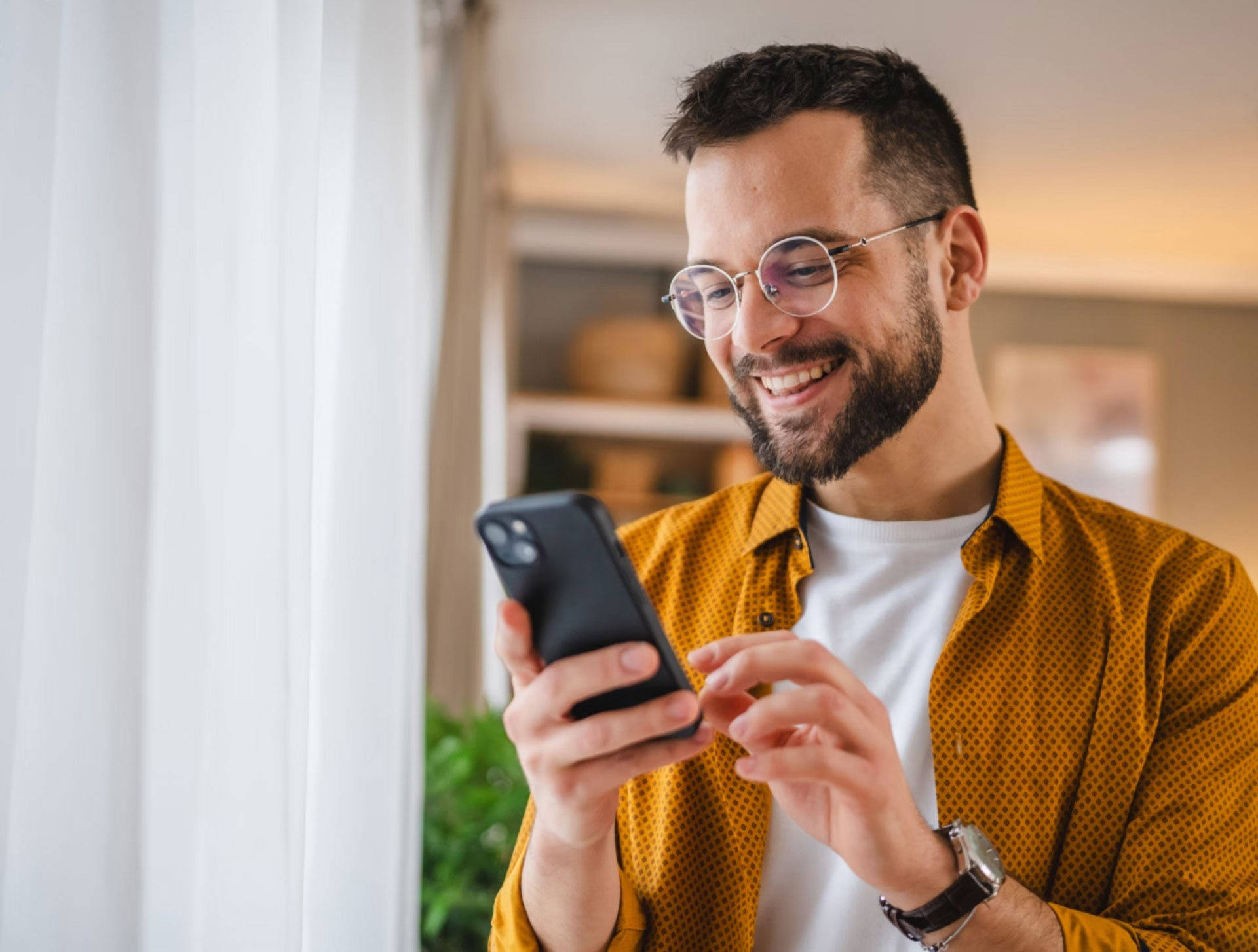 Mann schaut sich auf dem Handy etwas an und freut sich dabei.