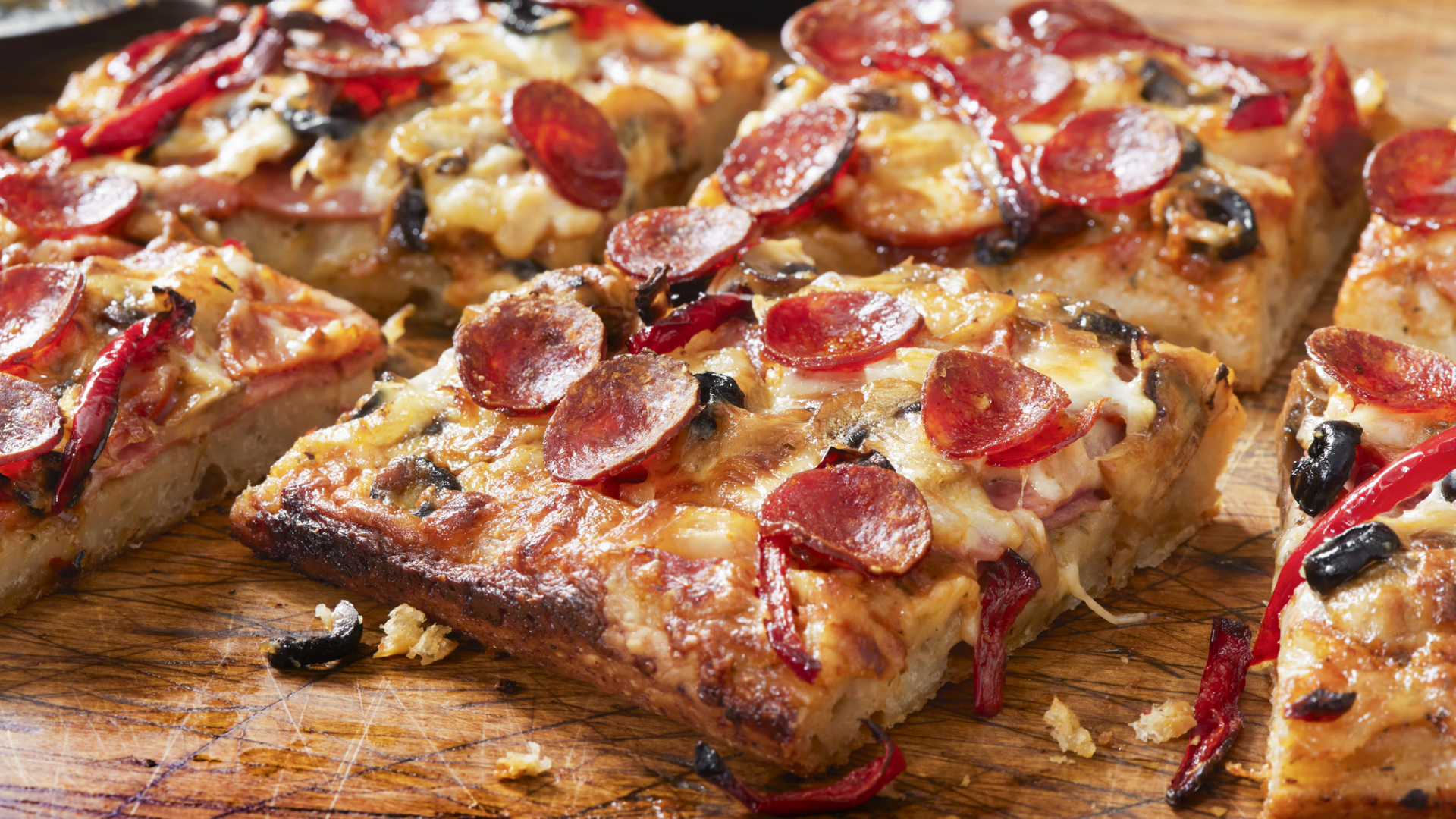 Pizzastücke mit Salami, Käse, Oliven und Paprika auf Holz.