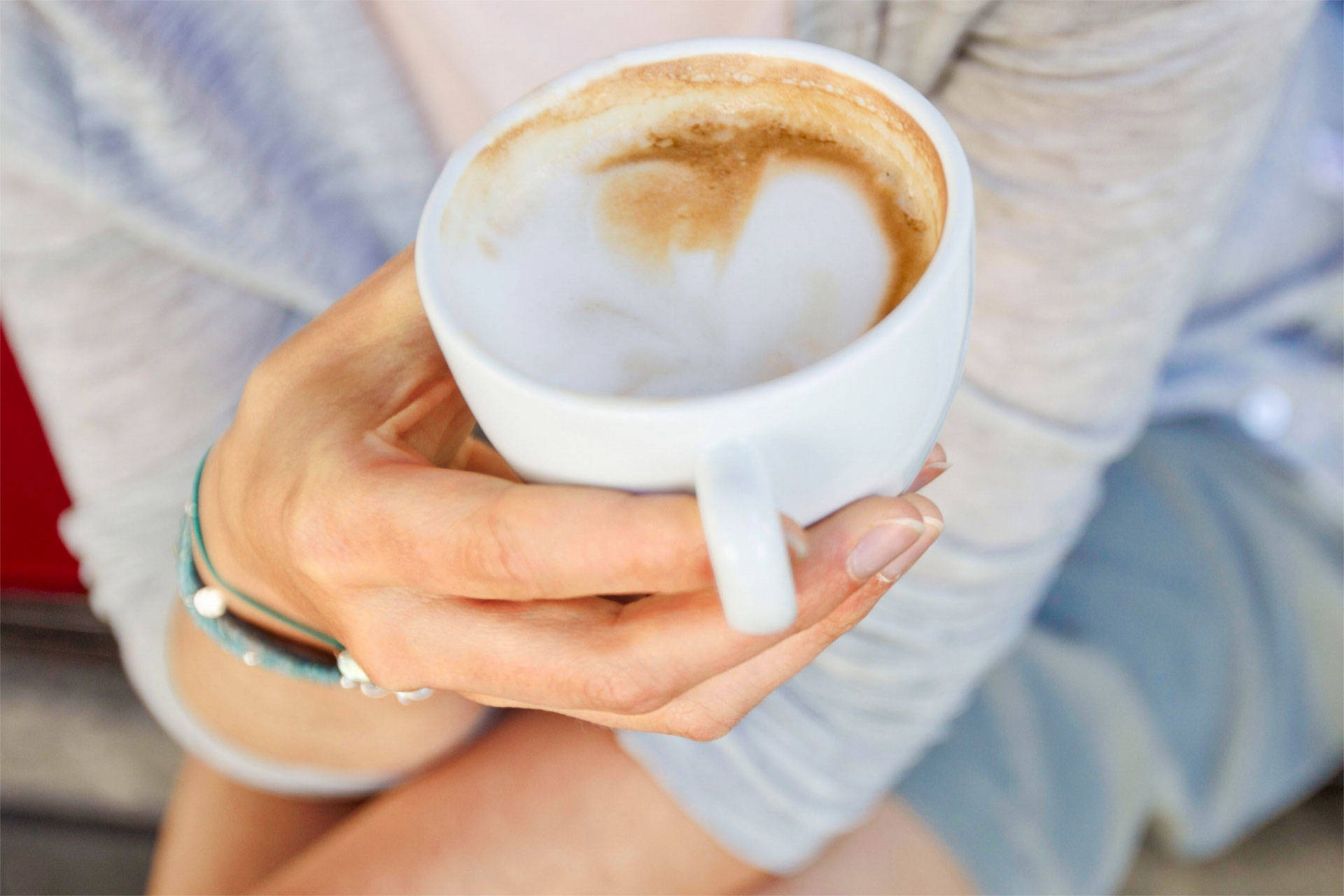 Eine Hand hält eine Tasse Cappuccino.