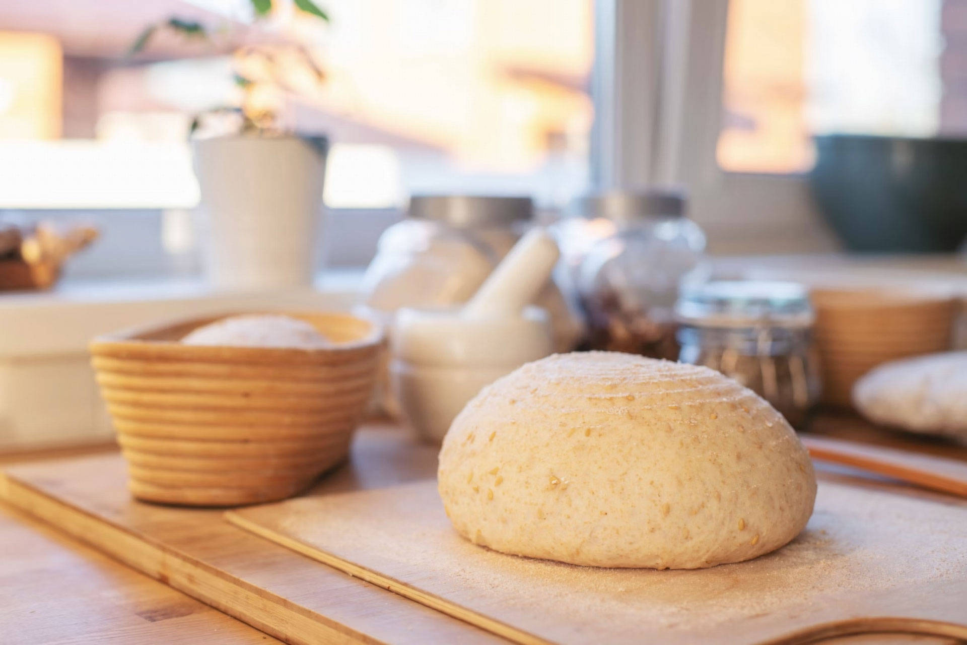 Rund geformter Sauerteig ruht auf einem Holzbrett in einer Küche am Fenster.