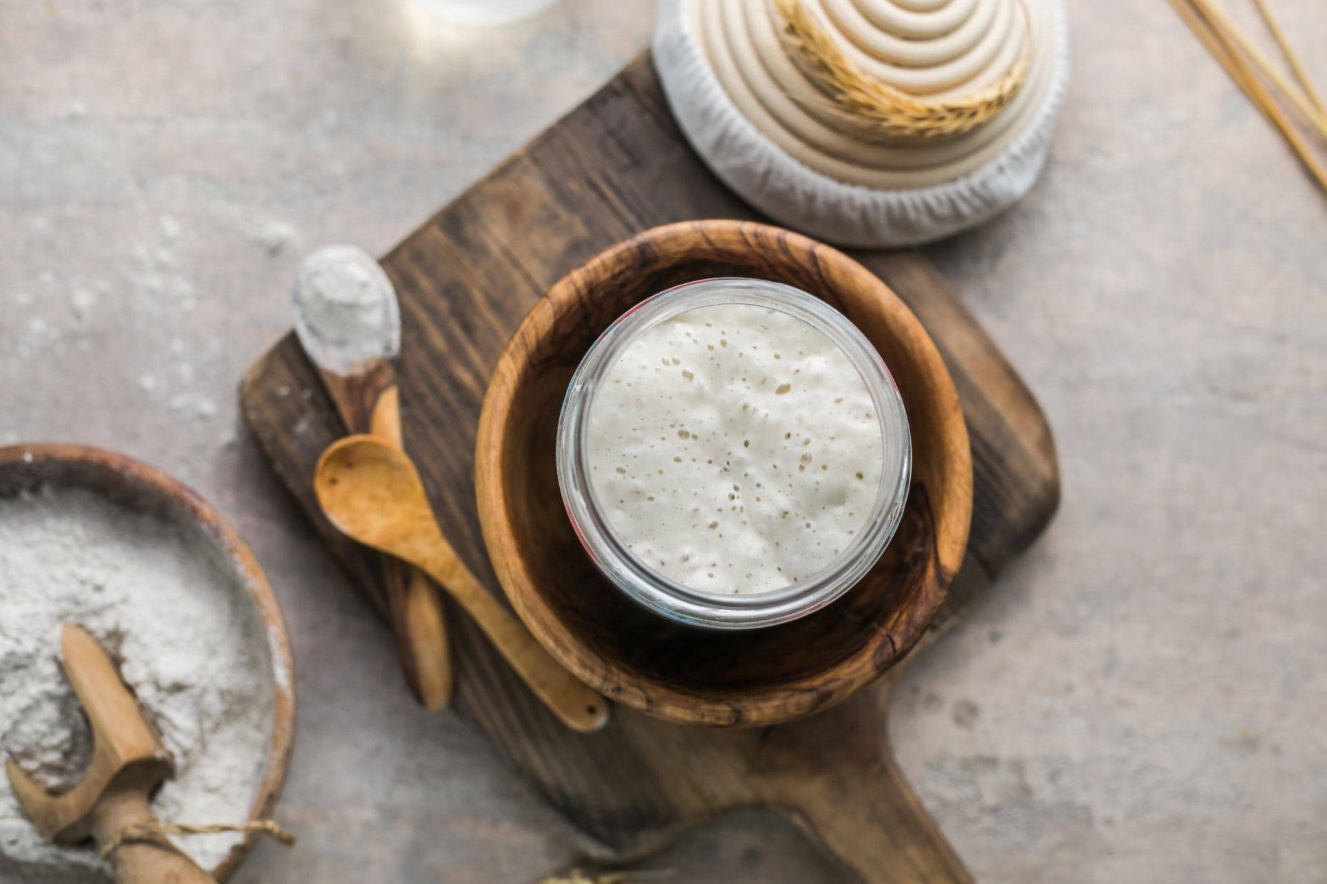 Ein Glas mit angesetztem Sauerteig, der Bläschen schlägt, auf einem Holzbrett.