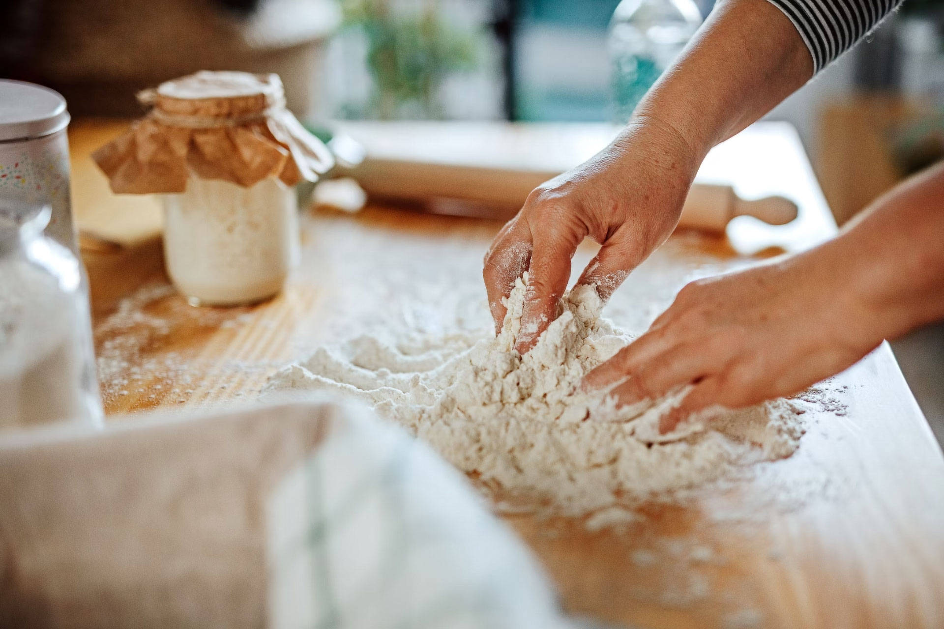 Person knetet Teig mit den Händen auf einer Holzunterlage.