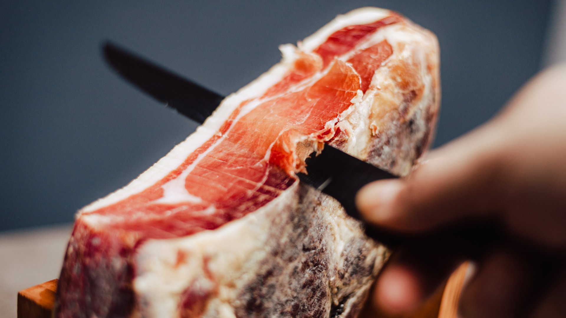 Hand schneidet dünne Scheibe von einem Schinken.