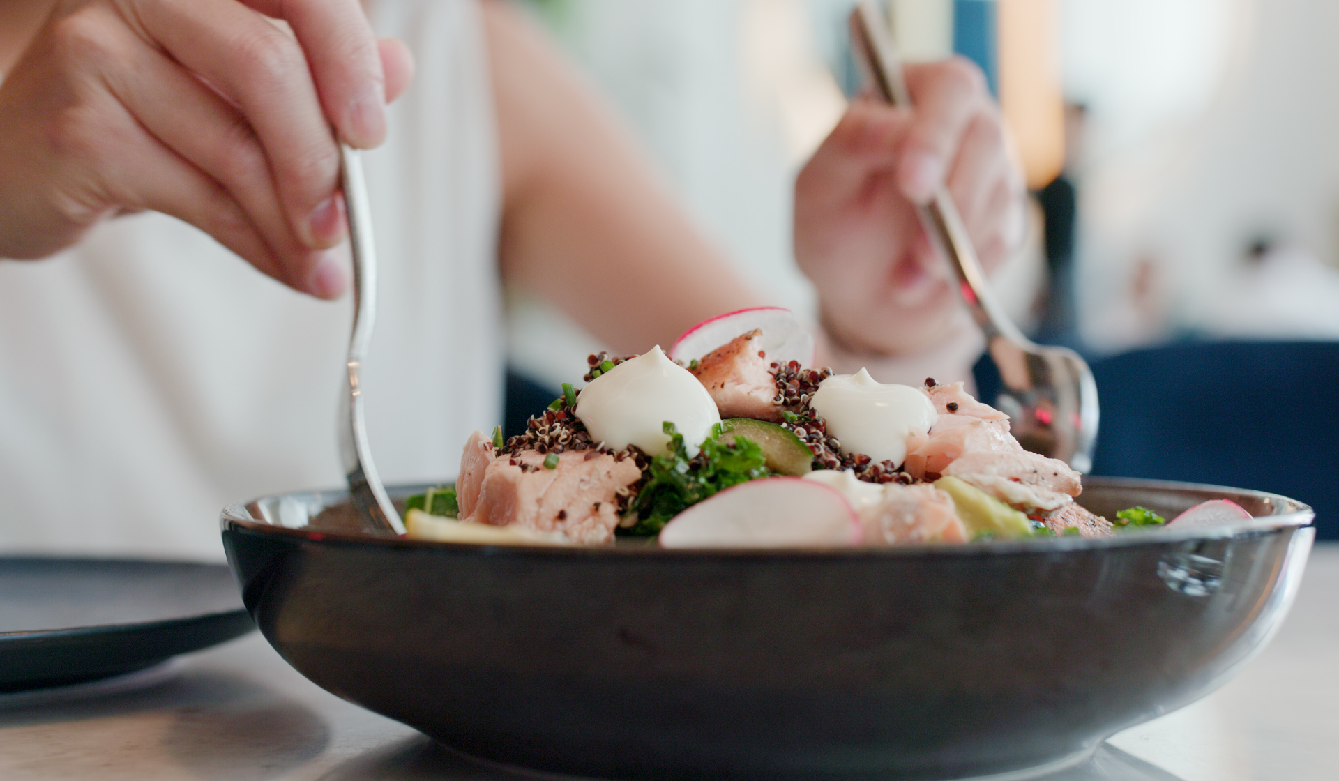 Eine Person mischt einen Salat in einer Porzellanschale.
