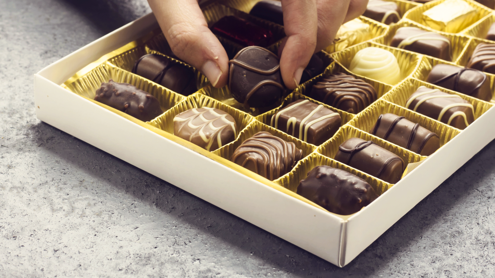 Pralinen in Schachtel, Hand nimmt Praline heraus.