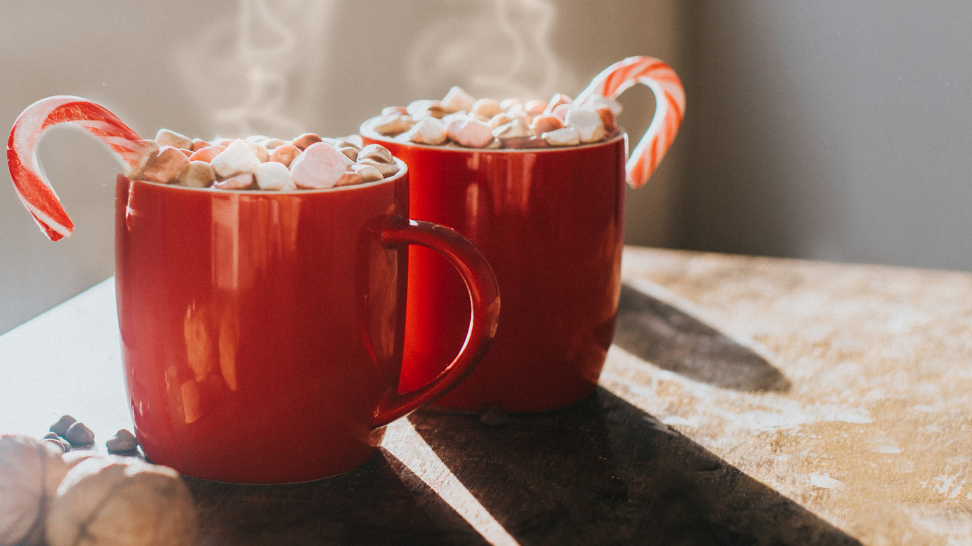 Zwei rote Tassen Schokomilch mit Marshmallows und Zuckerstange.