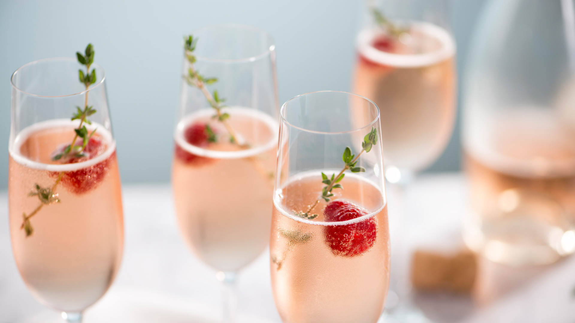 Gläser mit rosa Sekt, Himbeeren und Thymian.