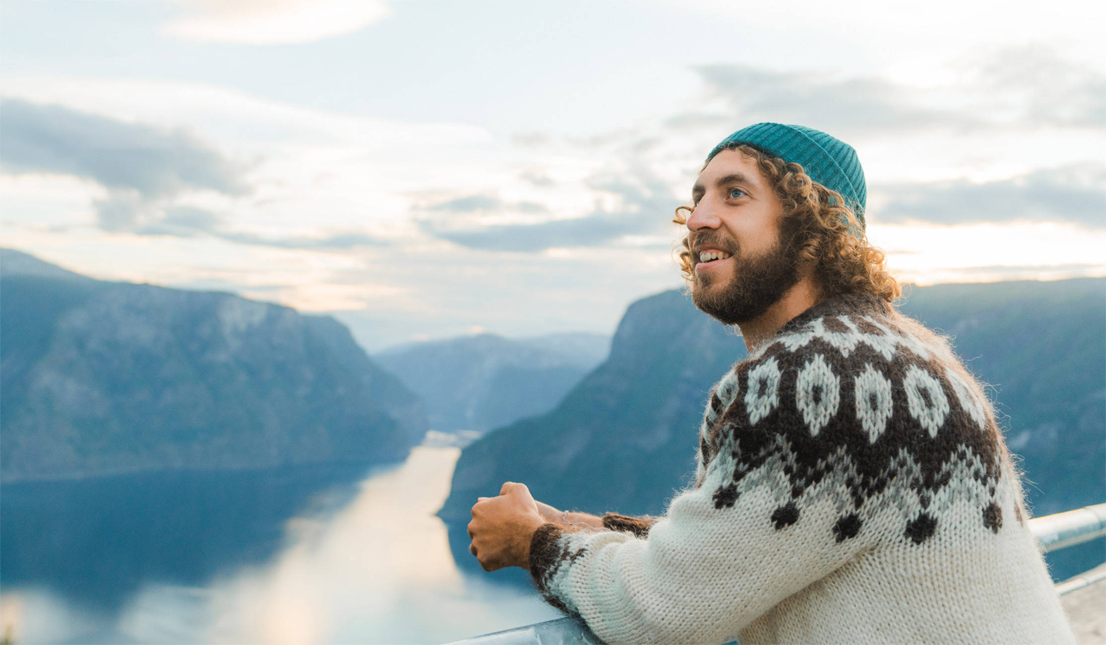 Ein lächelnder Mann steht oberhalb von einem Fjord.