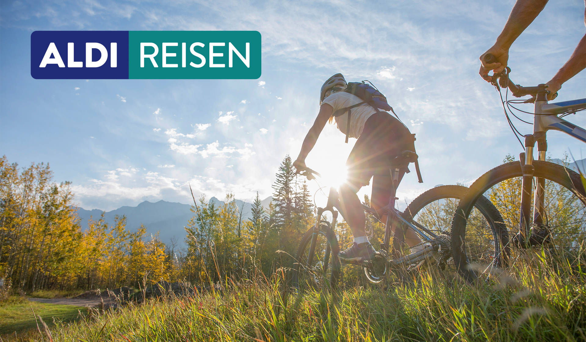 Zwei Menschen fahren mit ihrern Fahrrädern in den Bergen über eine Wiese.