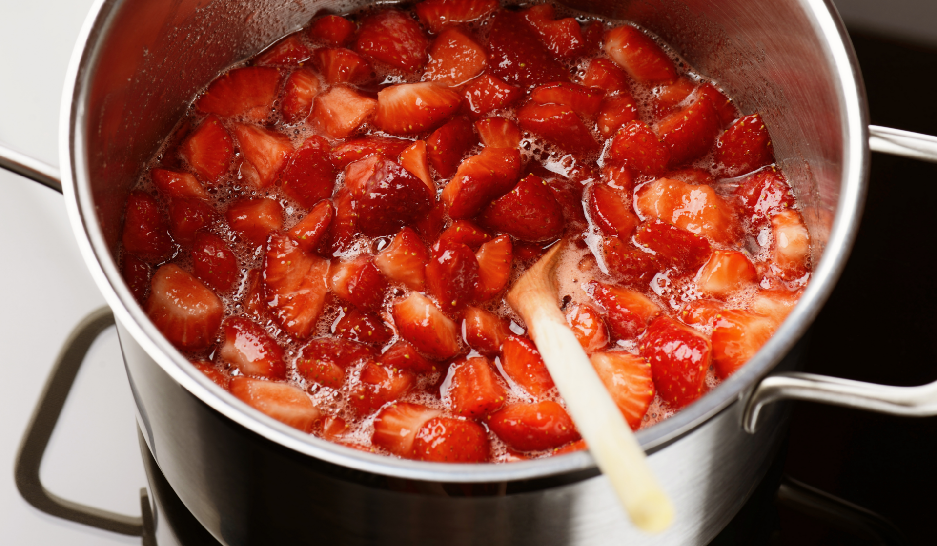 Erdbeeren köcheln im Topf mit Holzlöffel.
