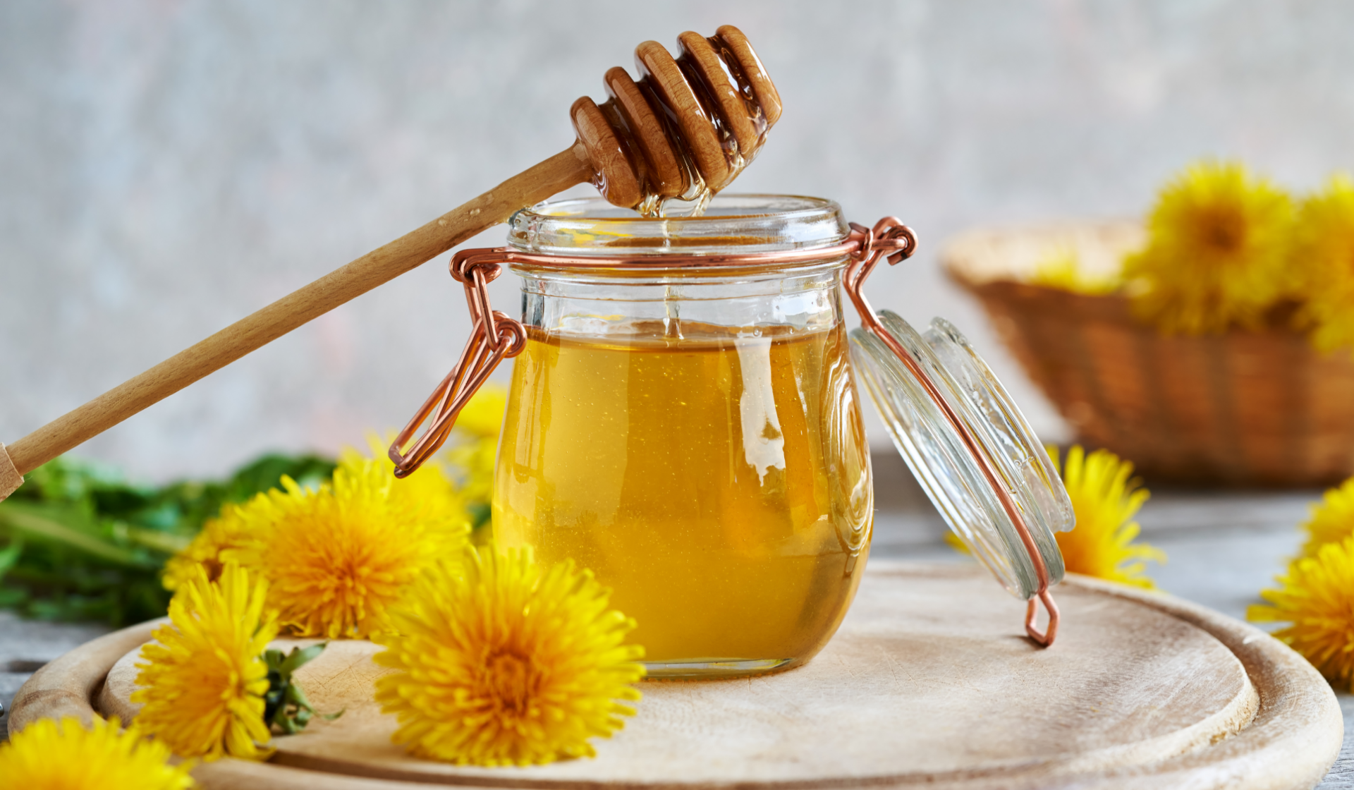 Löwenzahnsirup im Glas mit Honiglöffel und Löwenzahnblüten.