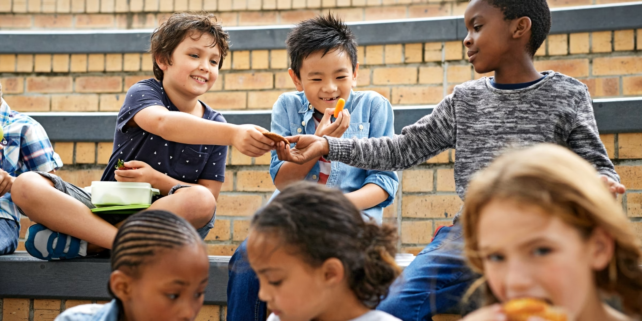 Kinder sitzen im Pausenhof und teilen sich freudig ihr Essen.