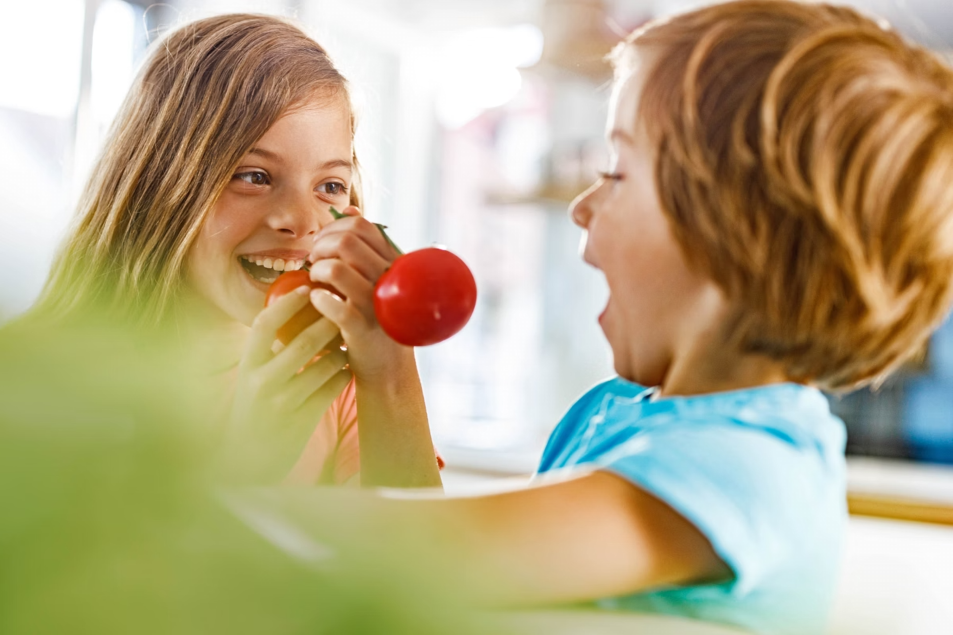 Zwei Kinder lachen und beißen in zwei rote Romaten.
