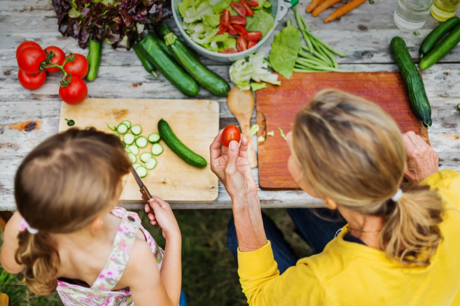 Eine Frau bereitet zusammen mit einem jungen Mädchen einen Salat im Freien zu.