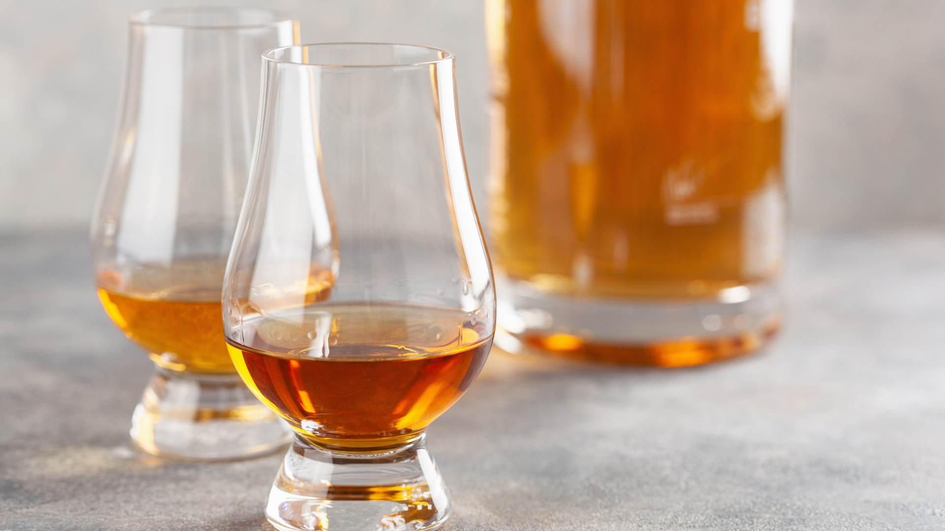Zwei Gläser mit Spirituosen, Flasche im Hintergrund.