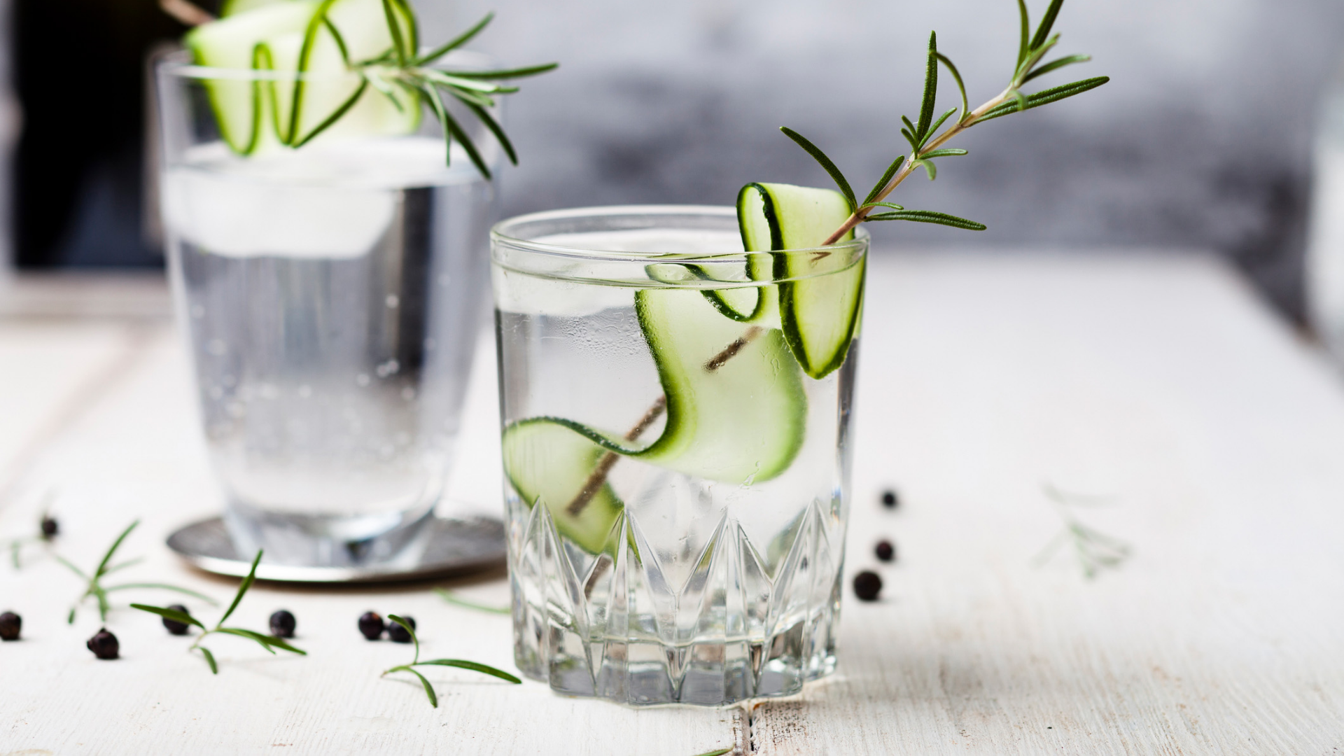 Gläser mit klarem Getränk, Gurke und Rosmarin.