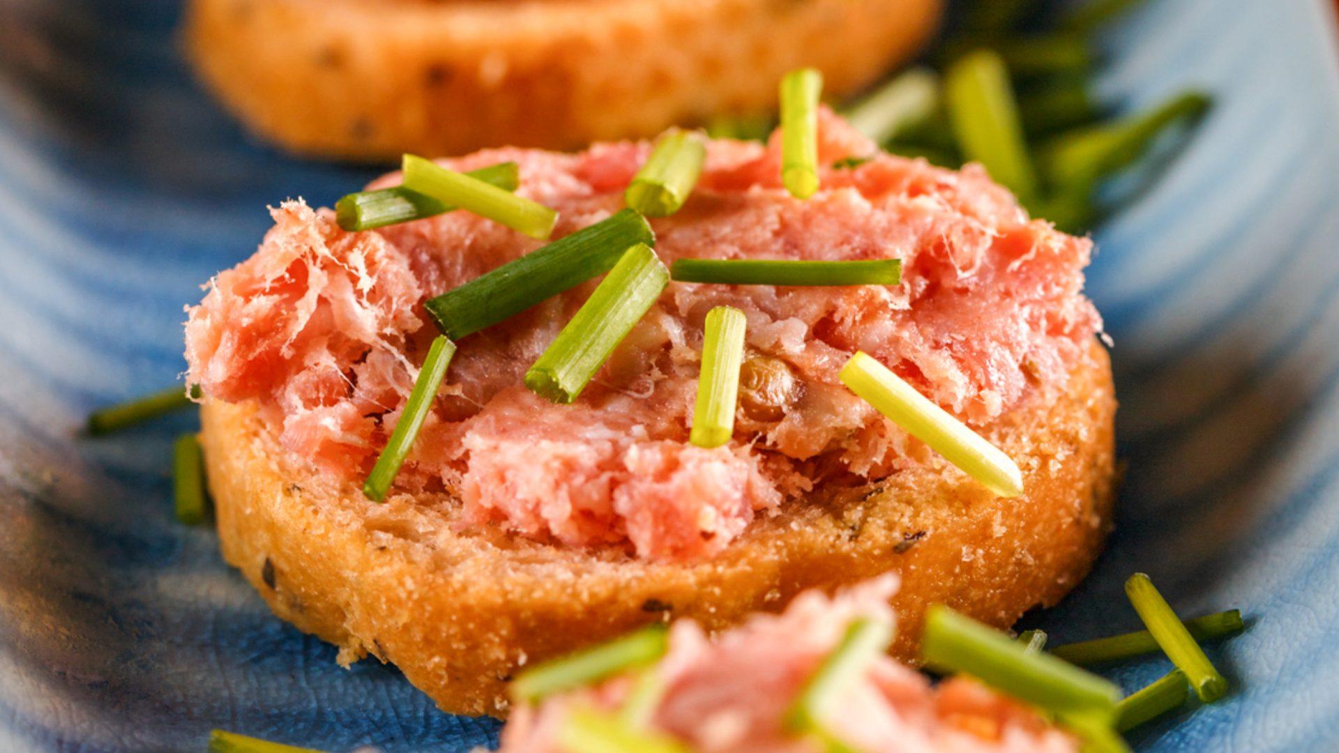 Brotstück mit rosa Wurstaufstrich und Schnittlauch.