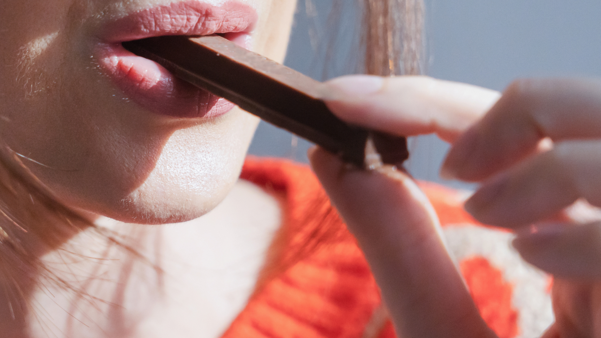 Frau isst Schokoladenriegel; Lippen und Hand im Fokus.
