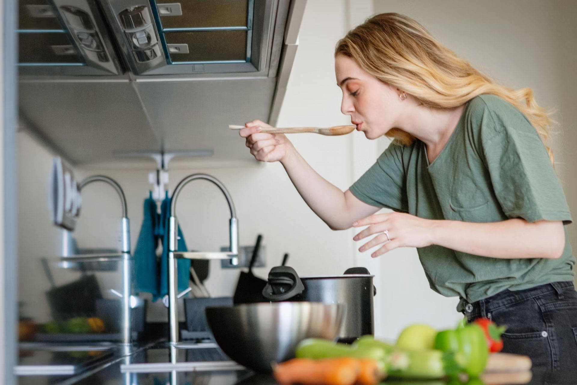 Frau probiert mit einem Holzlöffel ein Gericht aus einem Kochtopf in der Küche.
