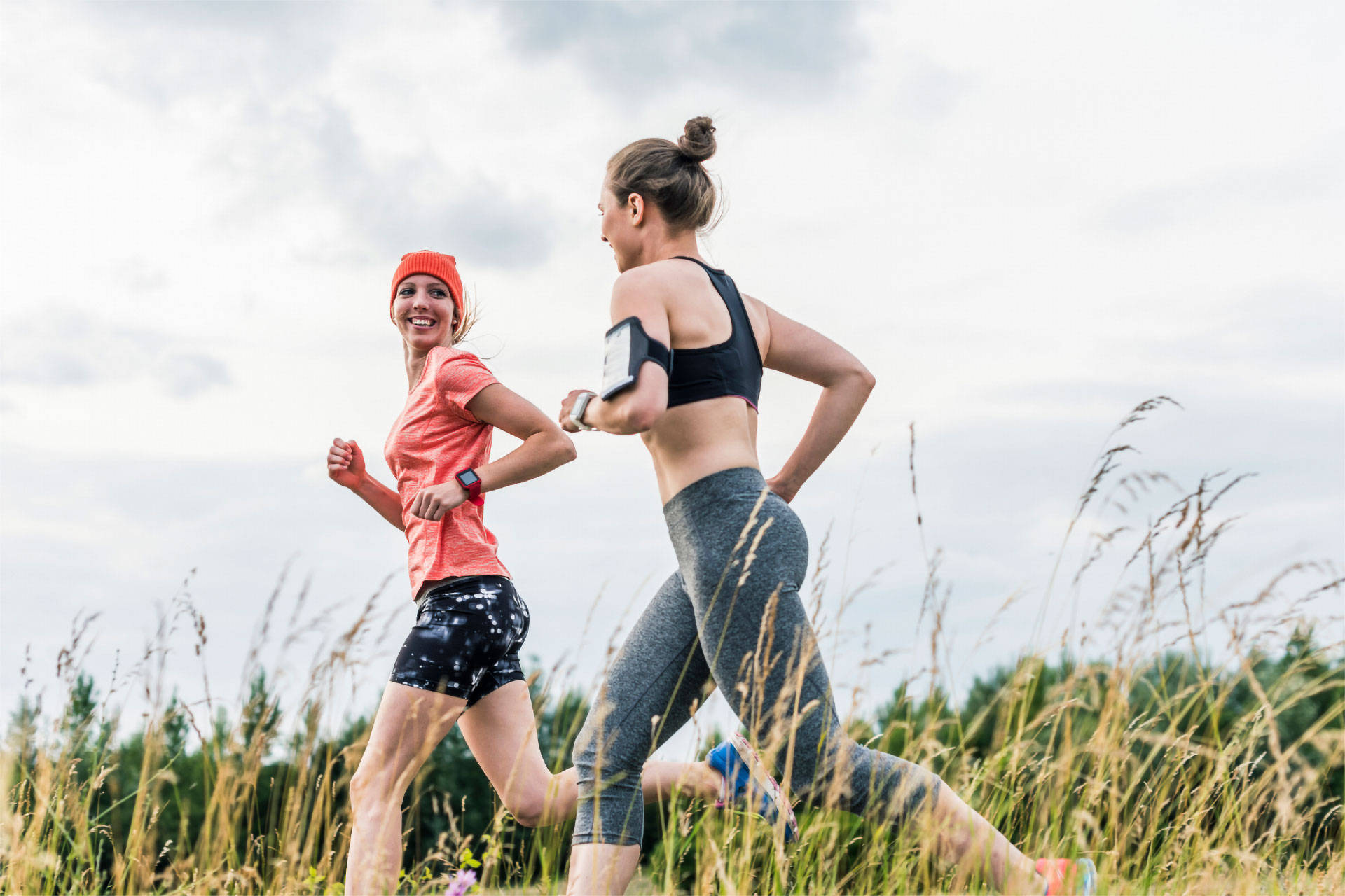 Zwei Frauen joggen gemeinsam durch ein Feld bei bewölktem Himmel.