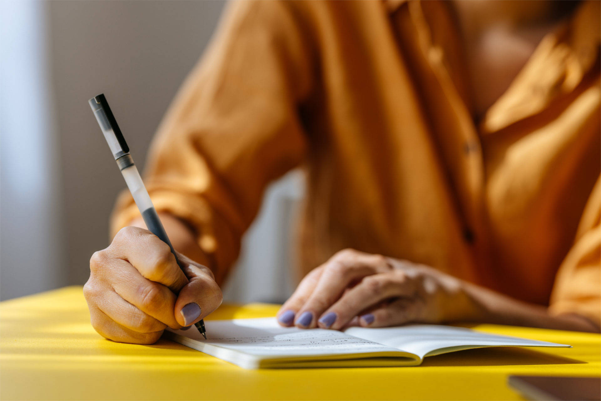 Person schreibt mit einem Stift Notizen in ein offenes Notizbuch.