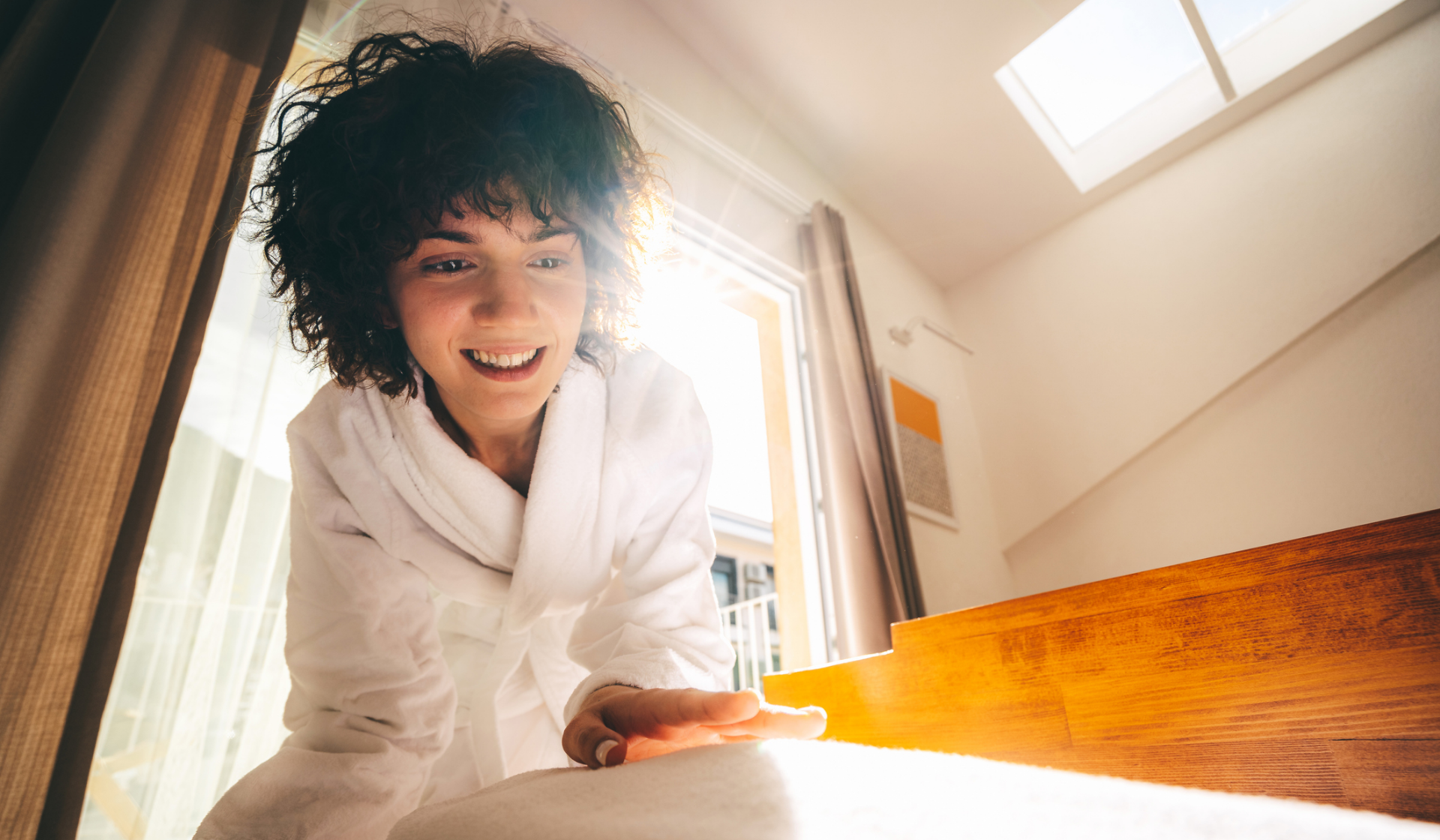 Lächelnde Frau im Bademantel bückt sich im Sonnenlicht.