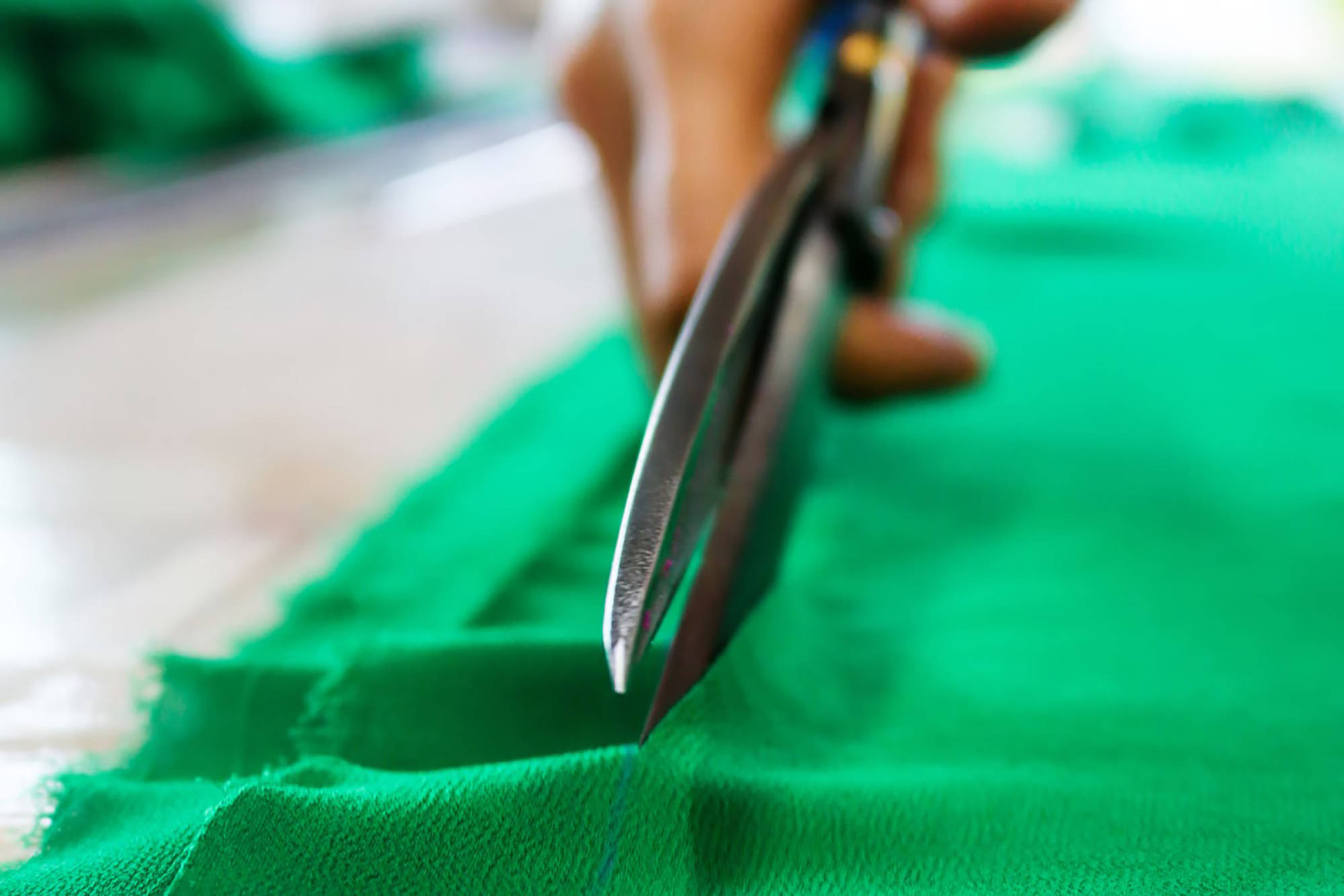 Eine Hand schneidet mit einer Stoffschere durch grünen Stoff.