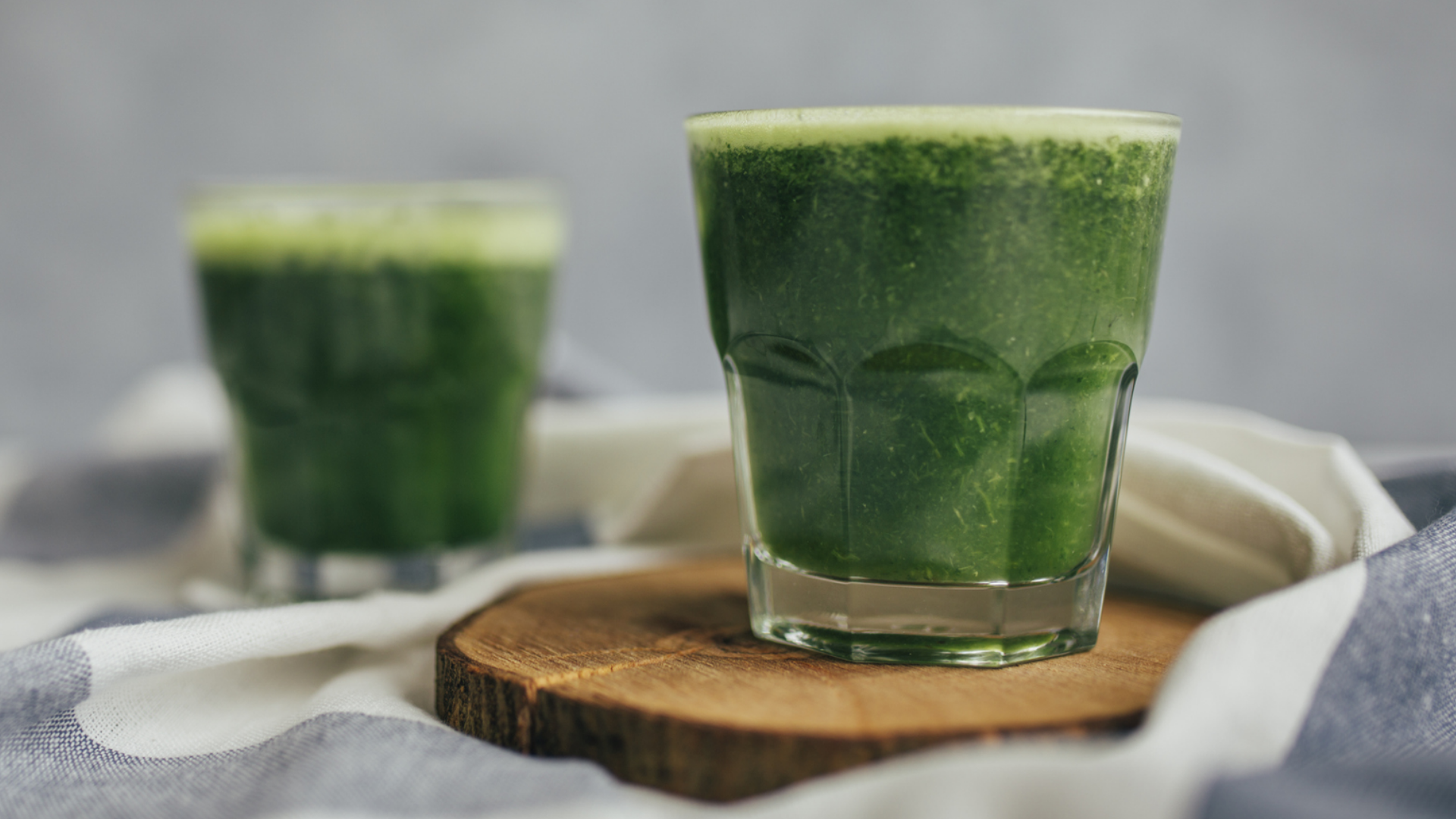 Zwei Gläser grüner Smoothie auf einem Holzteller.