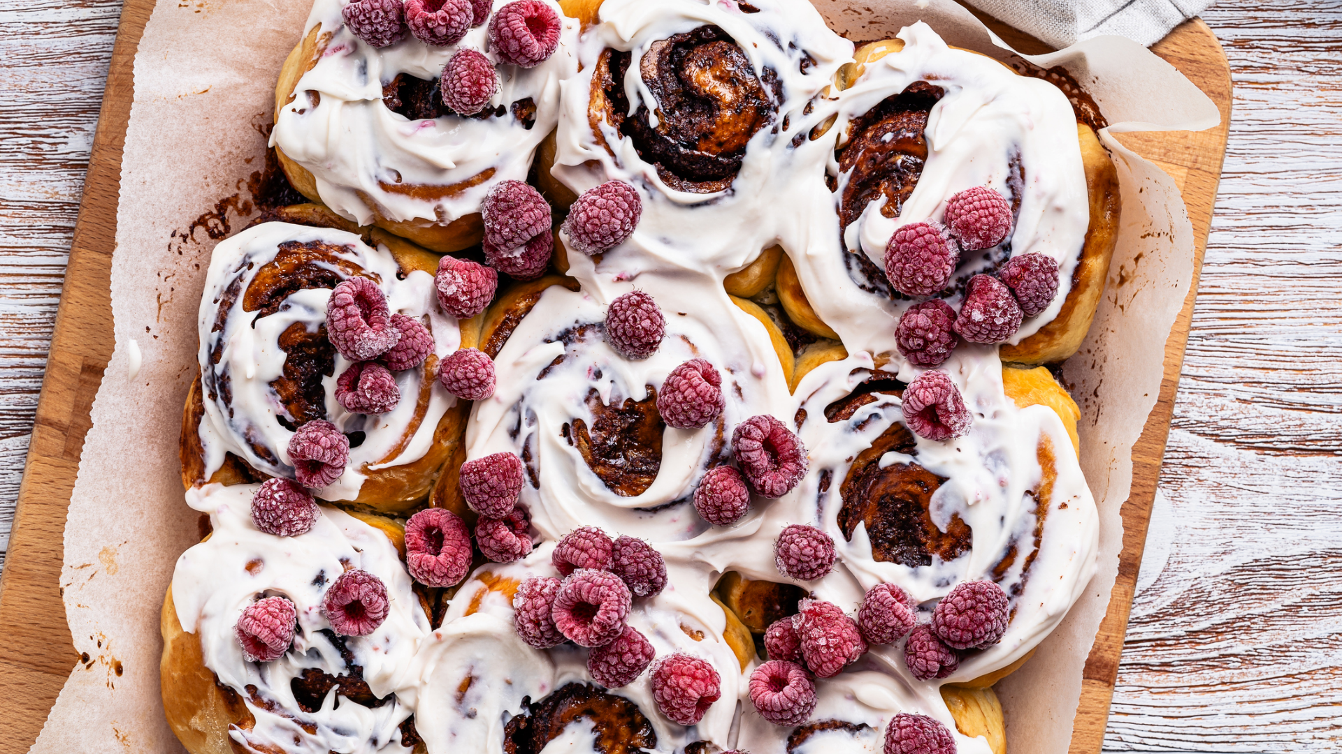 Zimtschnecken mit Frischkäse-Frosting und Himbeeren auf Holzbrett.
