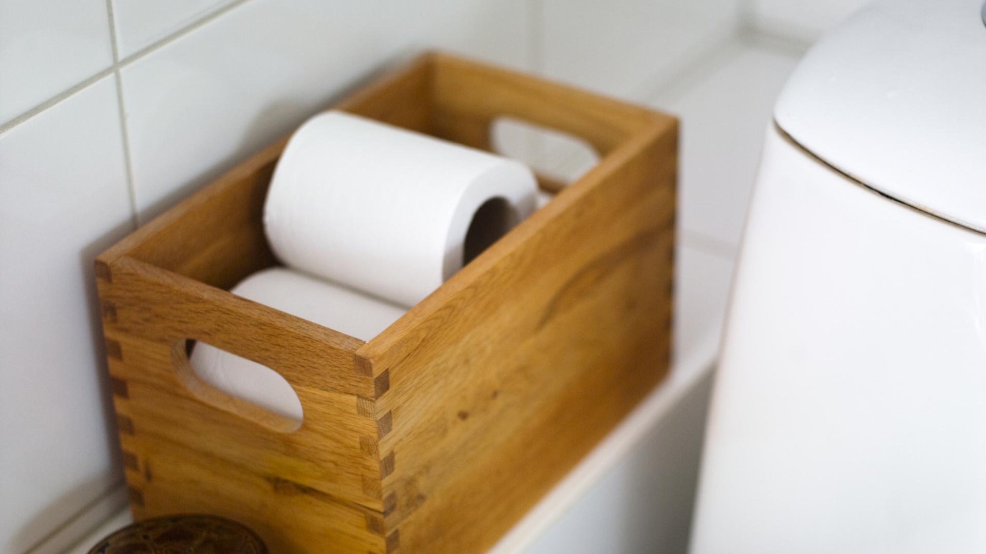 Toilettenpapierrollen in Holzkiste neben weißer Toilette.