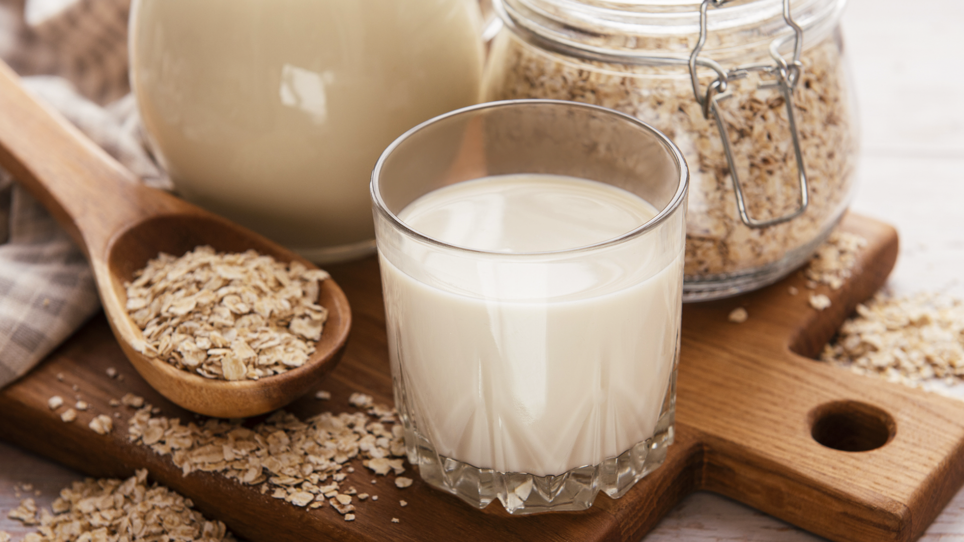 Glas Hafermilch und Haferflocken auf Holzbrett.