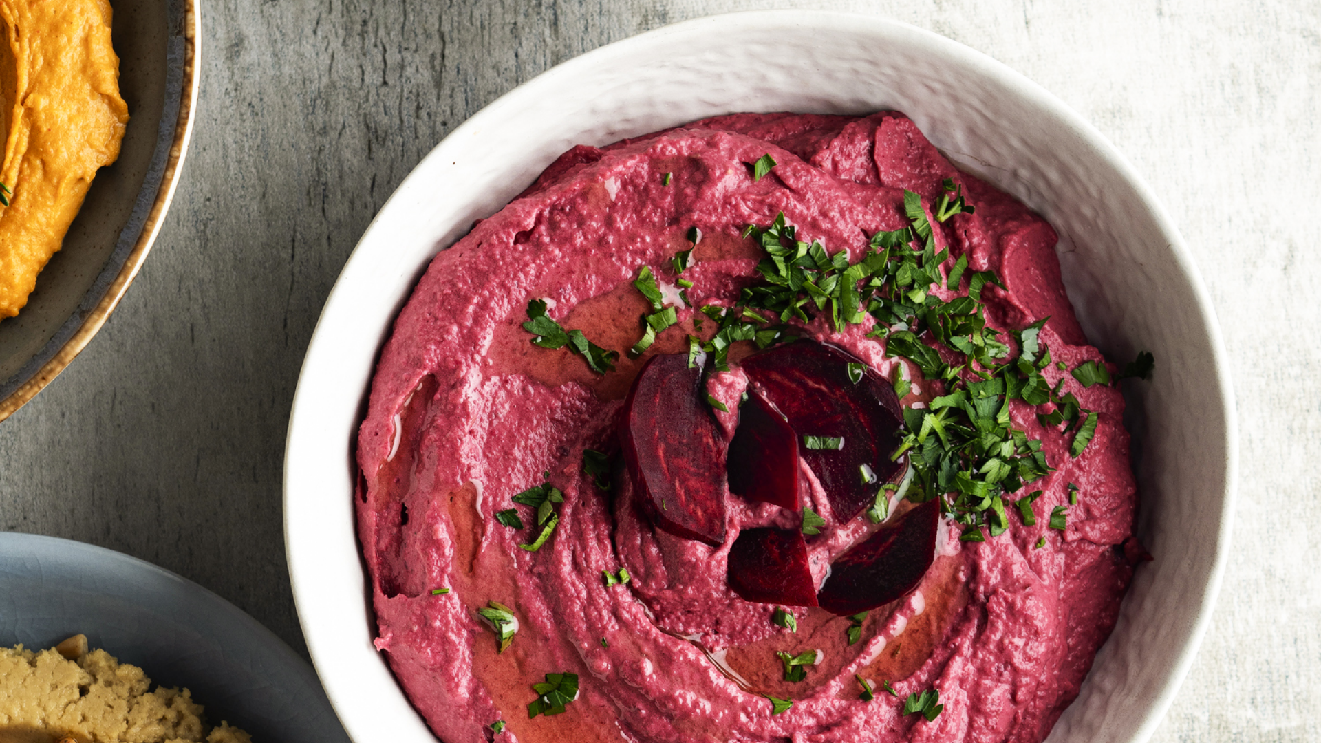 Schüssel mit pinkem Rote Bete Aufstrich, Kräutern und Öl.