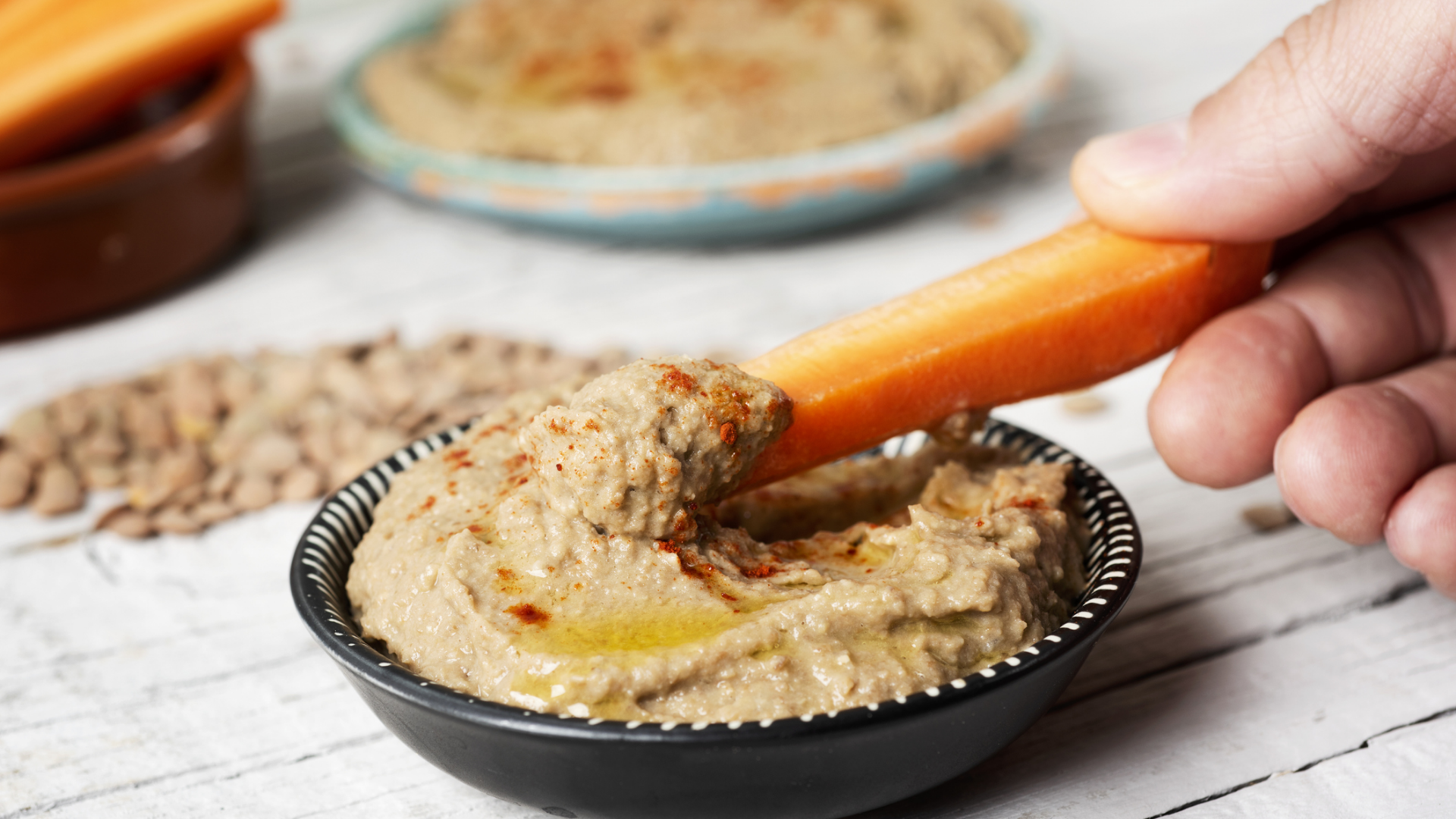 Karottenstück wird in veganen Aufstrich getaucht.