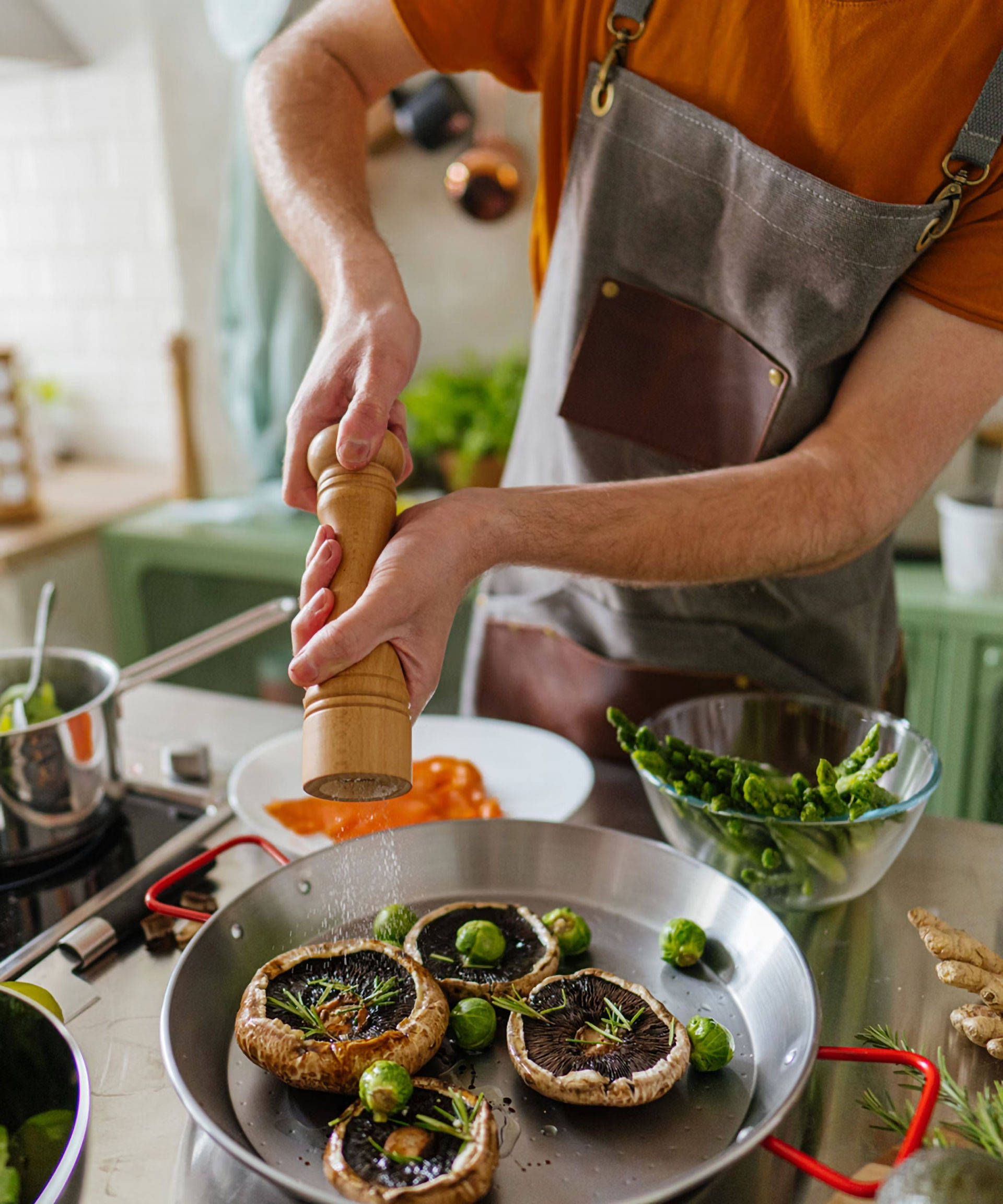 Person würzt Portobello-Pilze und Rosenkohl in einer Pfanne über dem Herd.