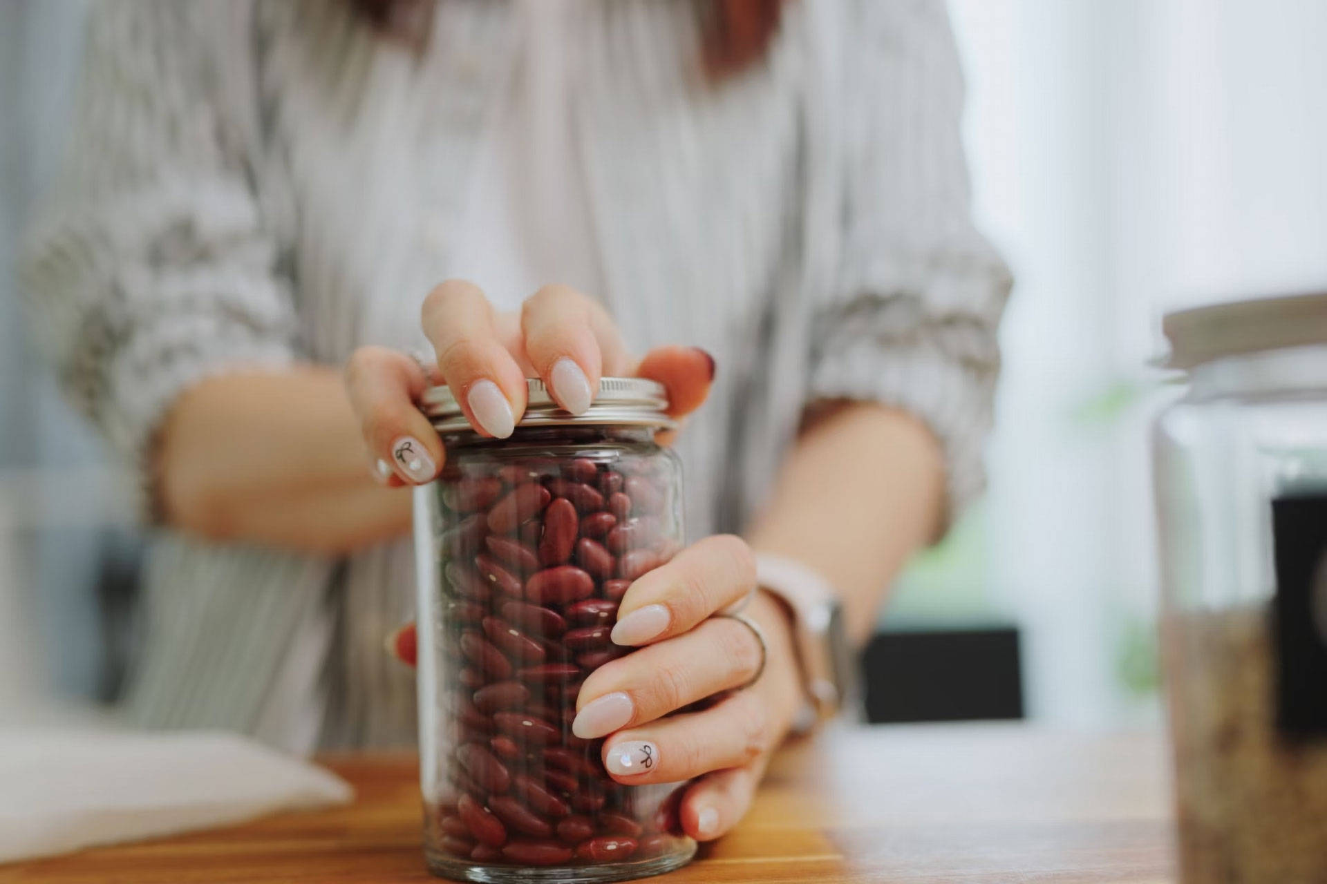 Frau öffnet ein Glas mit roten Kidneybohnen auf dem Tisch.