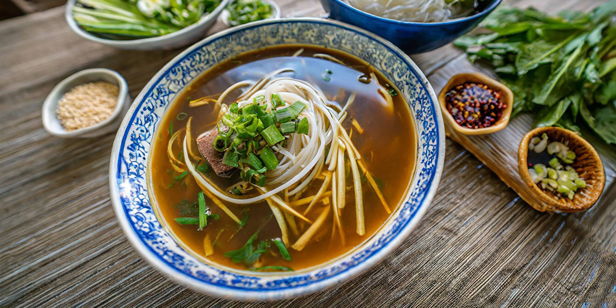 Vietnamesische Pho-Nudelsuppe mit Rindfleisch und Beilagen auf Holztisch.