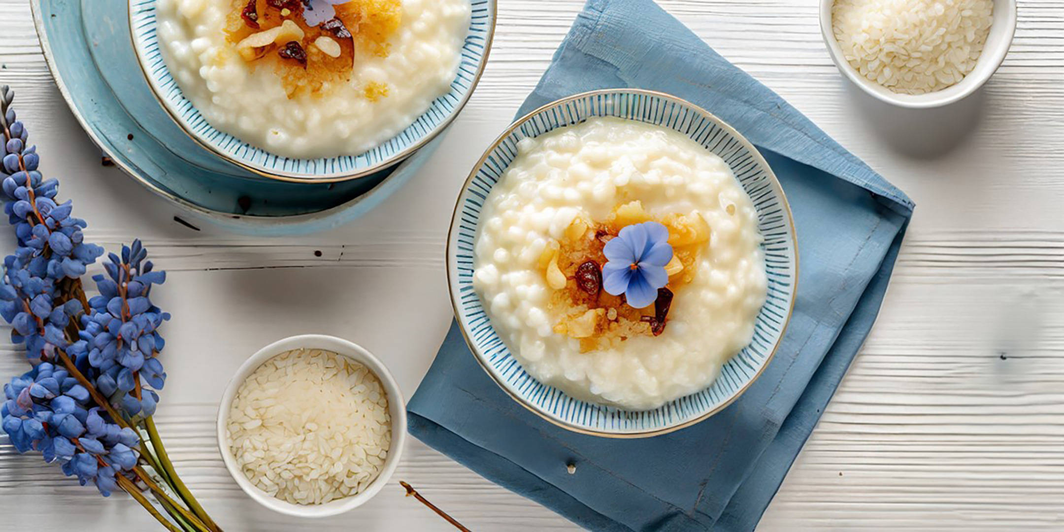 Zwei Schalen Milchreis mit Früchten, Rosinen und blauer Blüte.