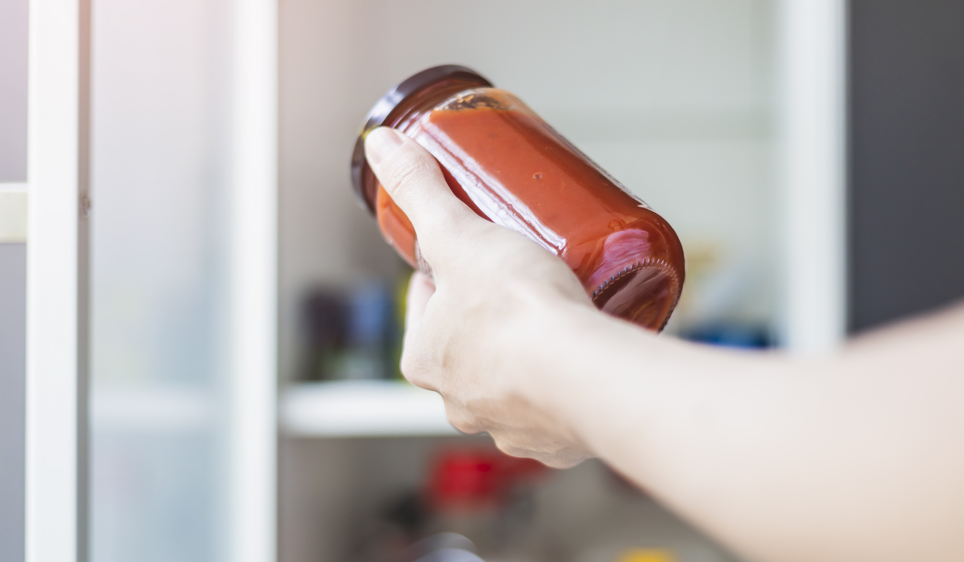 Eine Hand hält Tomatensoßen im Vorratsglas.