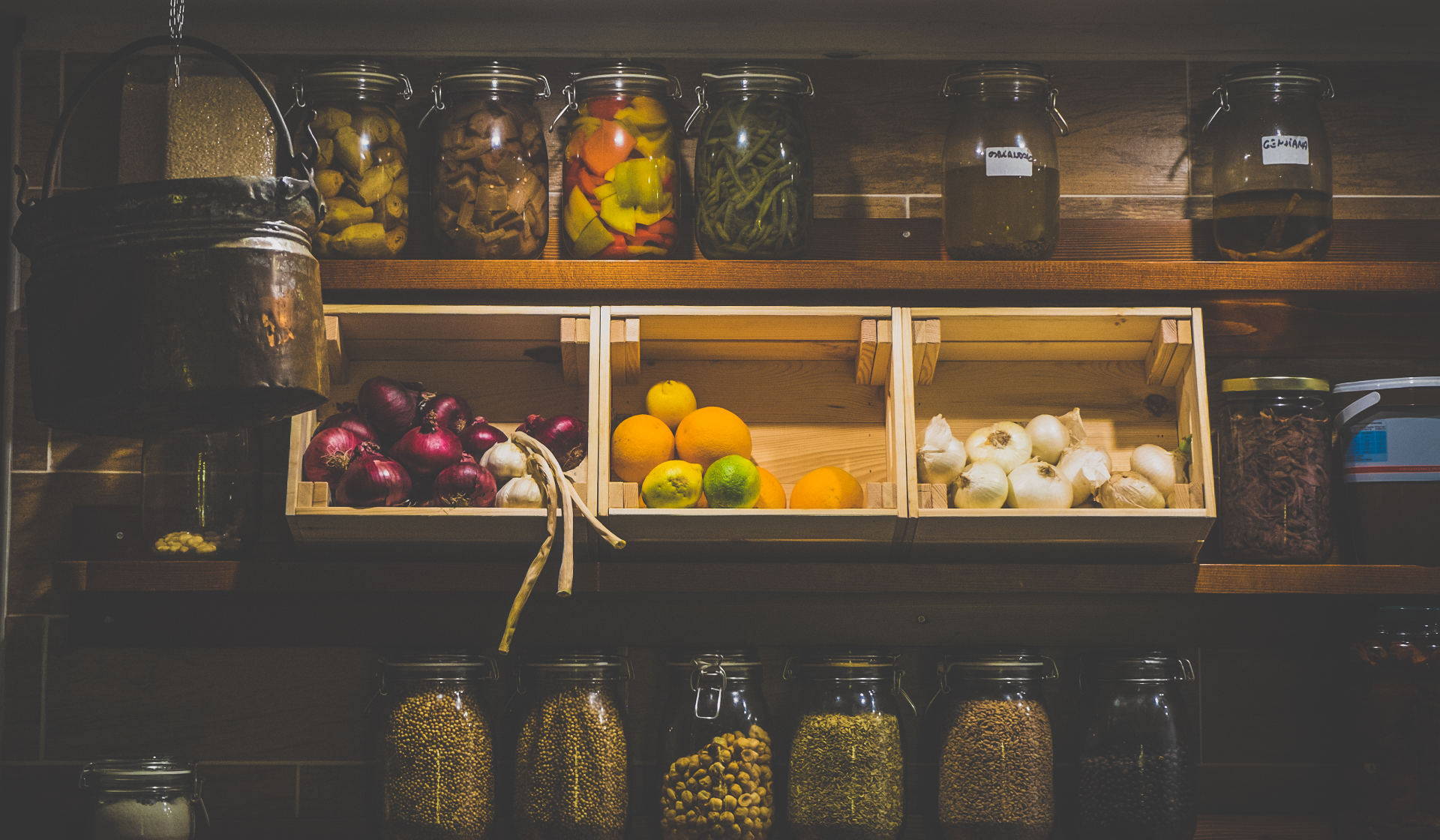 Dunkle Vorratskammer und drei hell erleuchtete Holzkisten mit Zwiebeln, Knoblauch und Zitronen, Orangen und Limetten.