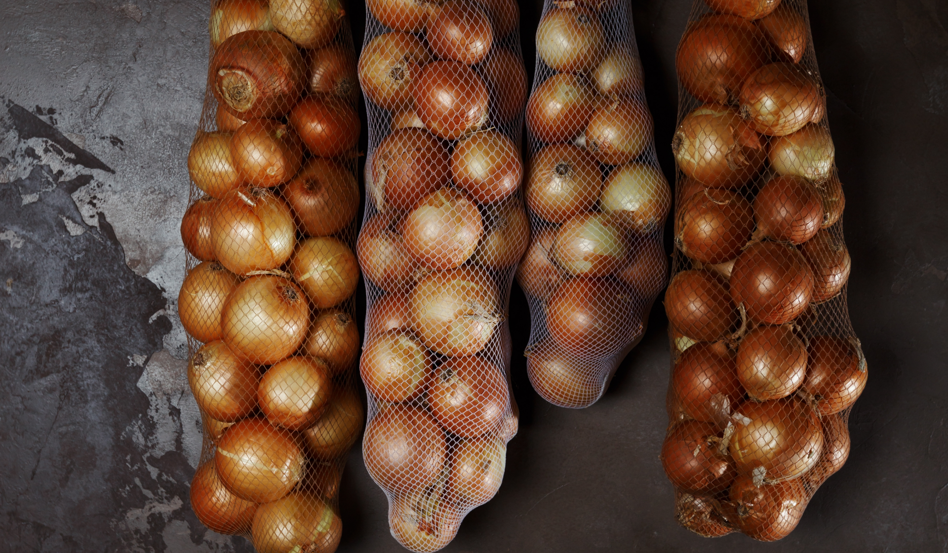 Zwiebeln im Vorratsnetz hängen in einem dunklen Raum.