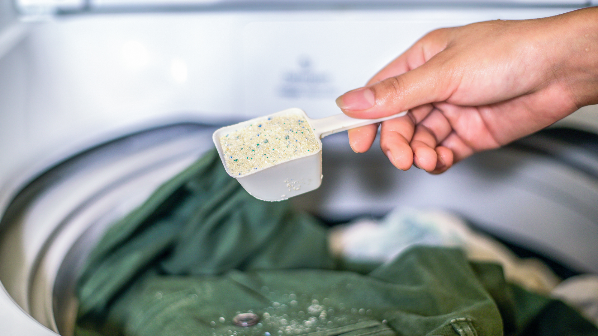 Hand füllt Waschpulver in Waschmaschine zur Wäsche.